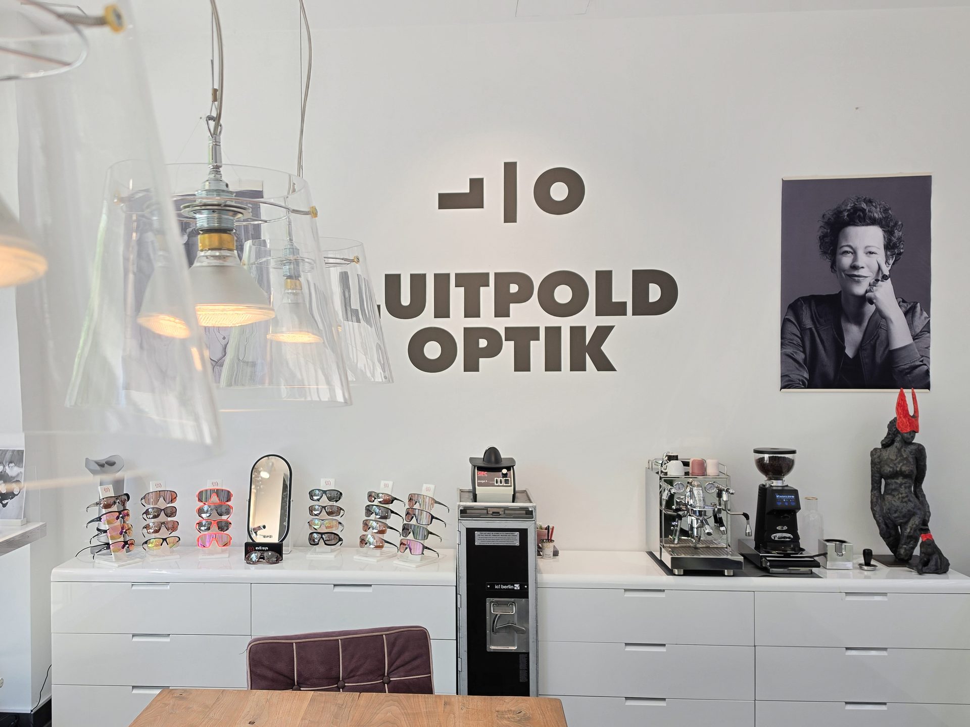 Interior of Uitpold Optik with eyeglass displays, coffee bar, and logo on a white wall.