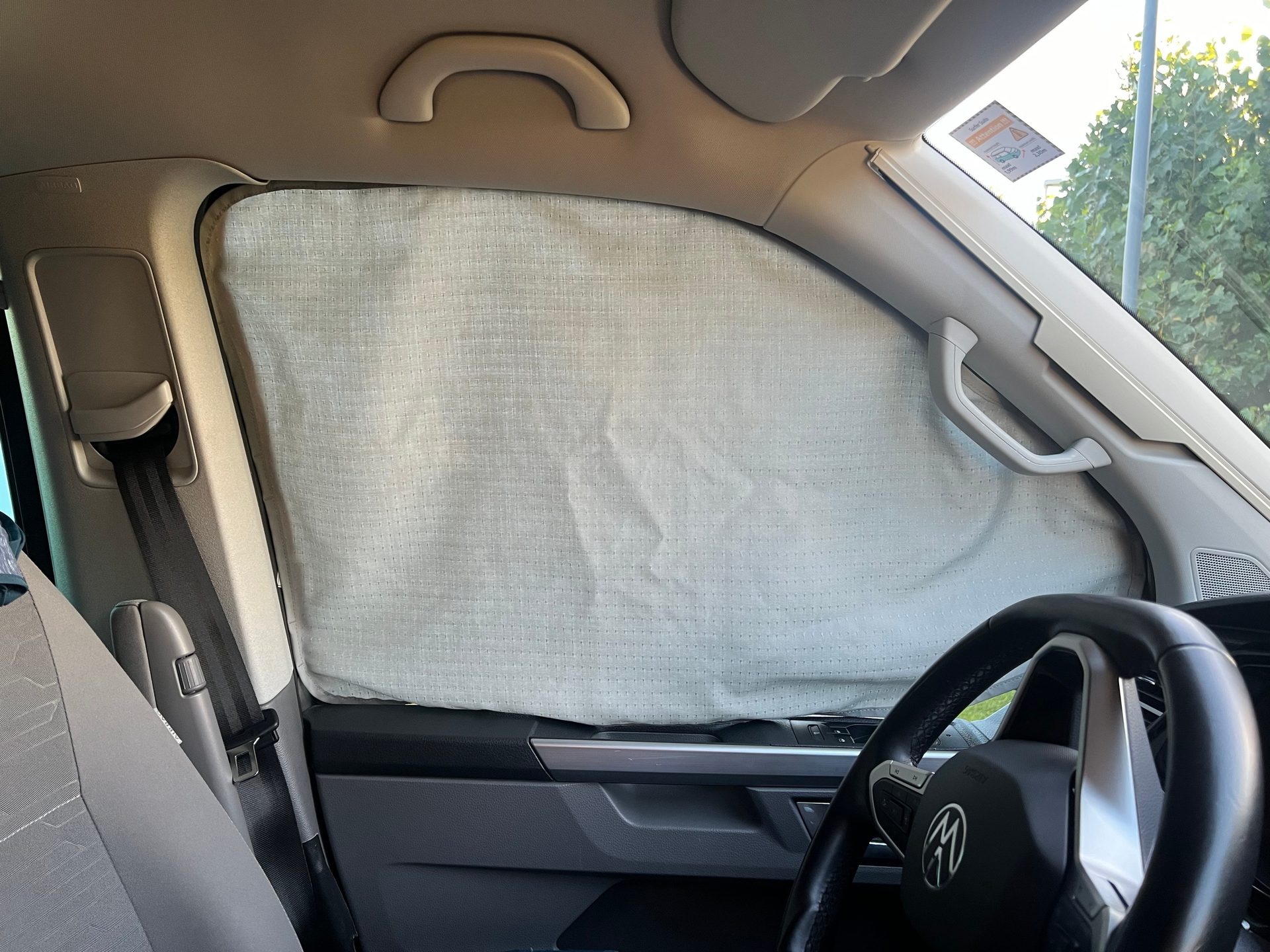 Car interior with window sunshade, steering wheel, and seatbelt.