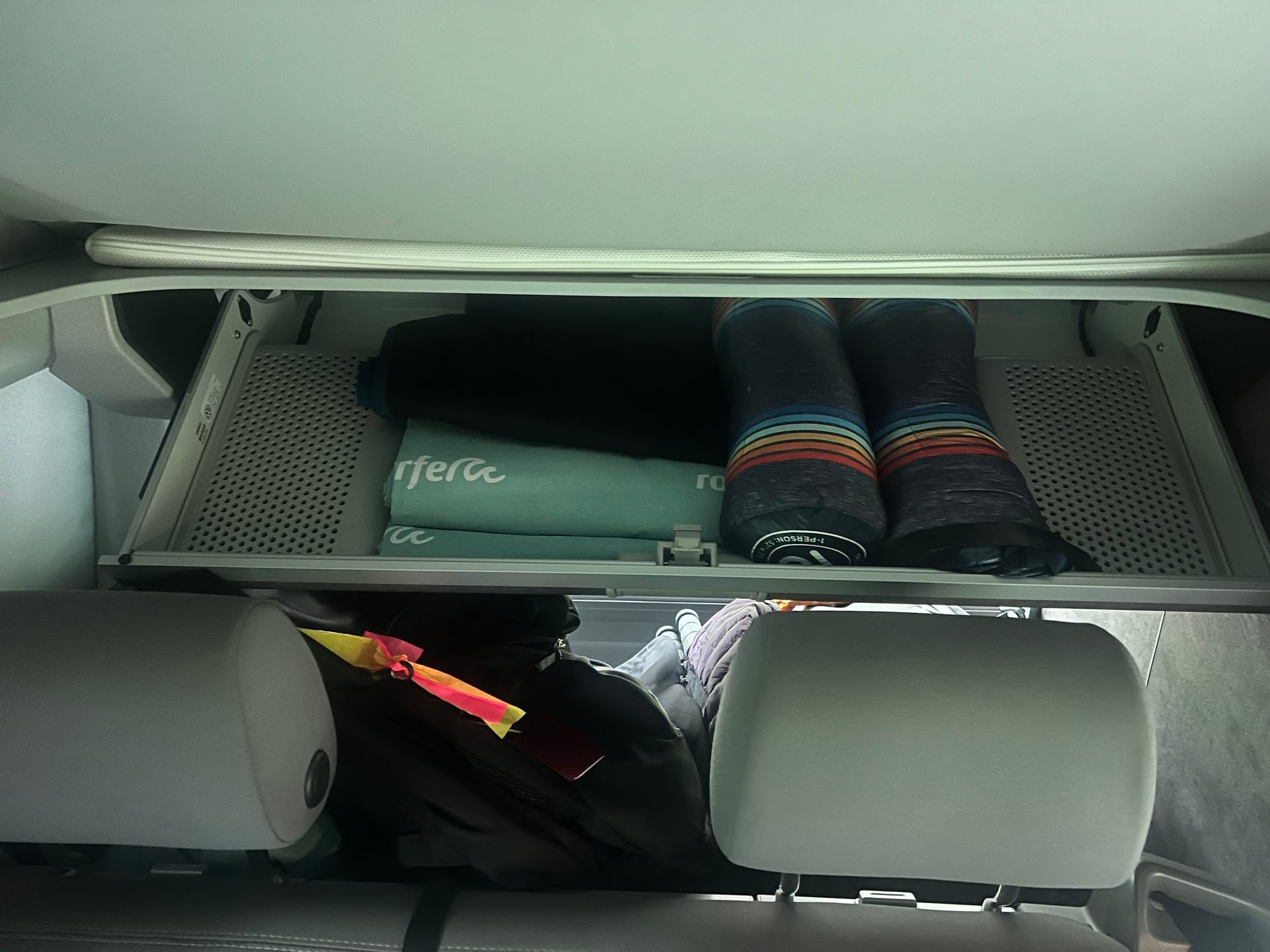 Overhead car storage with folded items and bags on seats below.