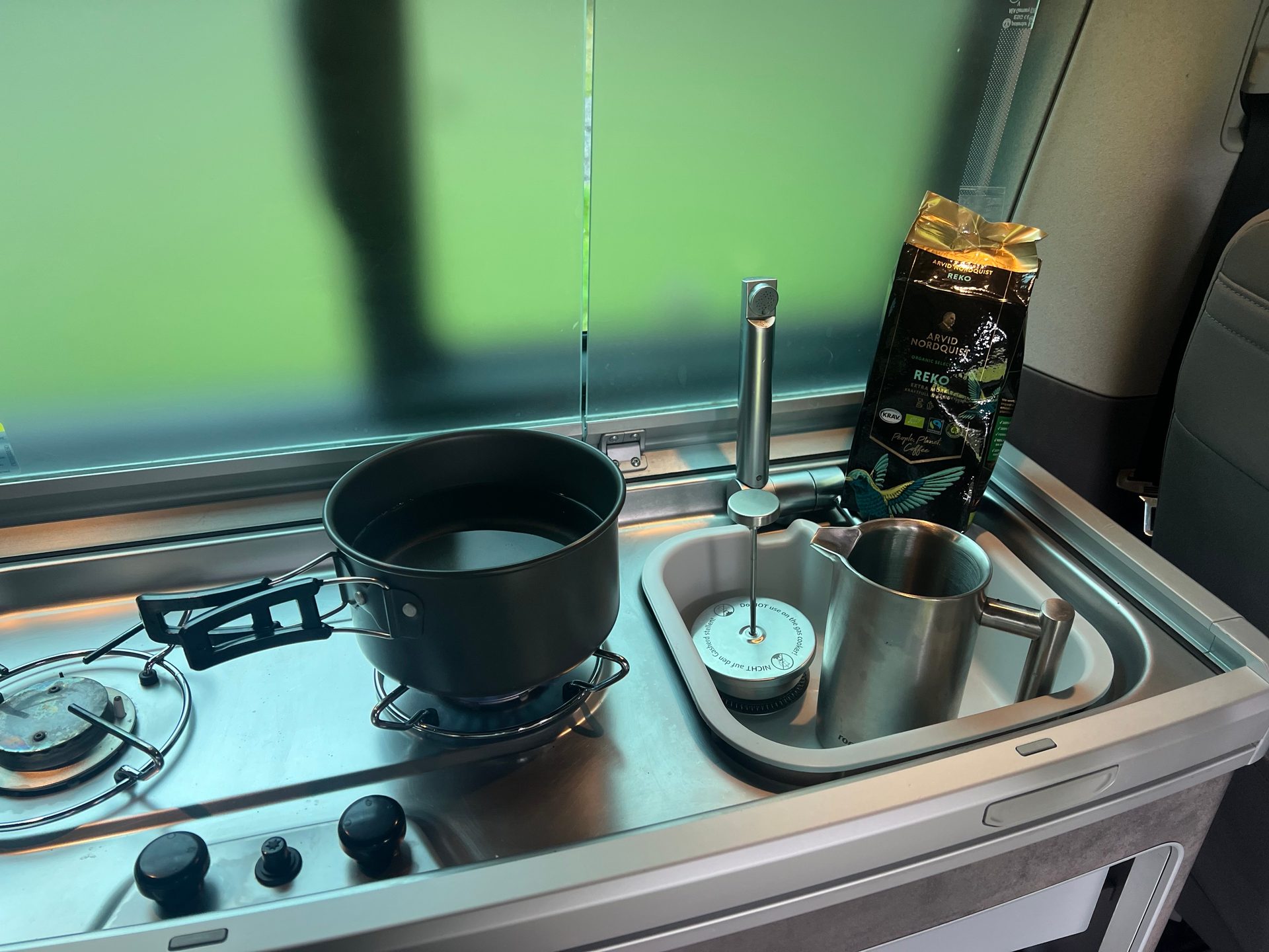 Campervan kitchen: pot on stove, sink with metal cup, and coffee bag.