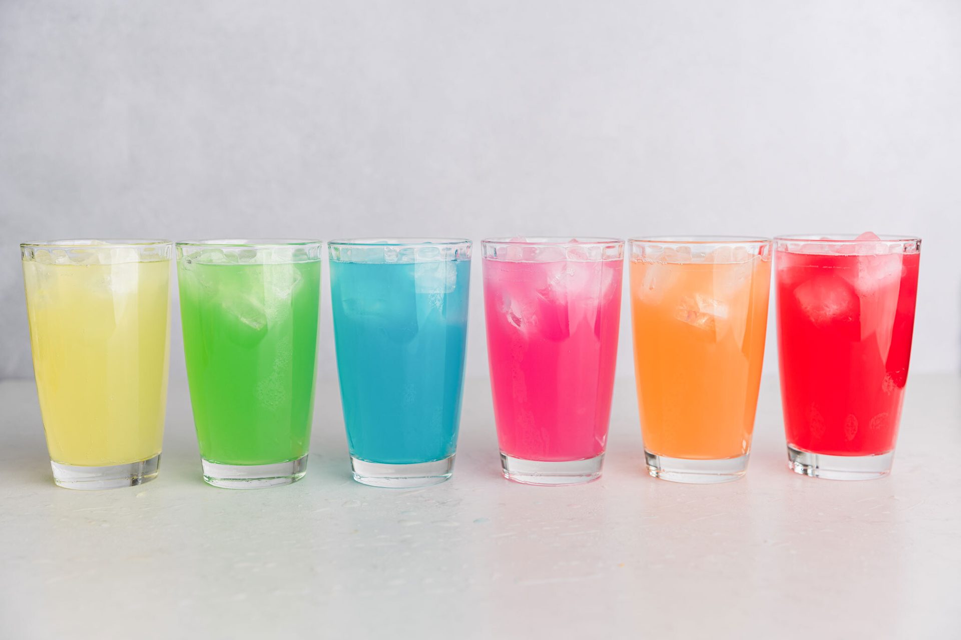 Six glasses of rainbow-colored iced drinks.