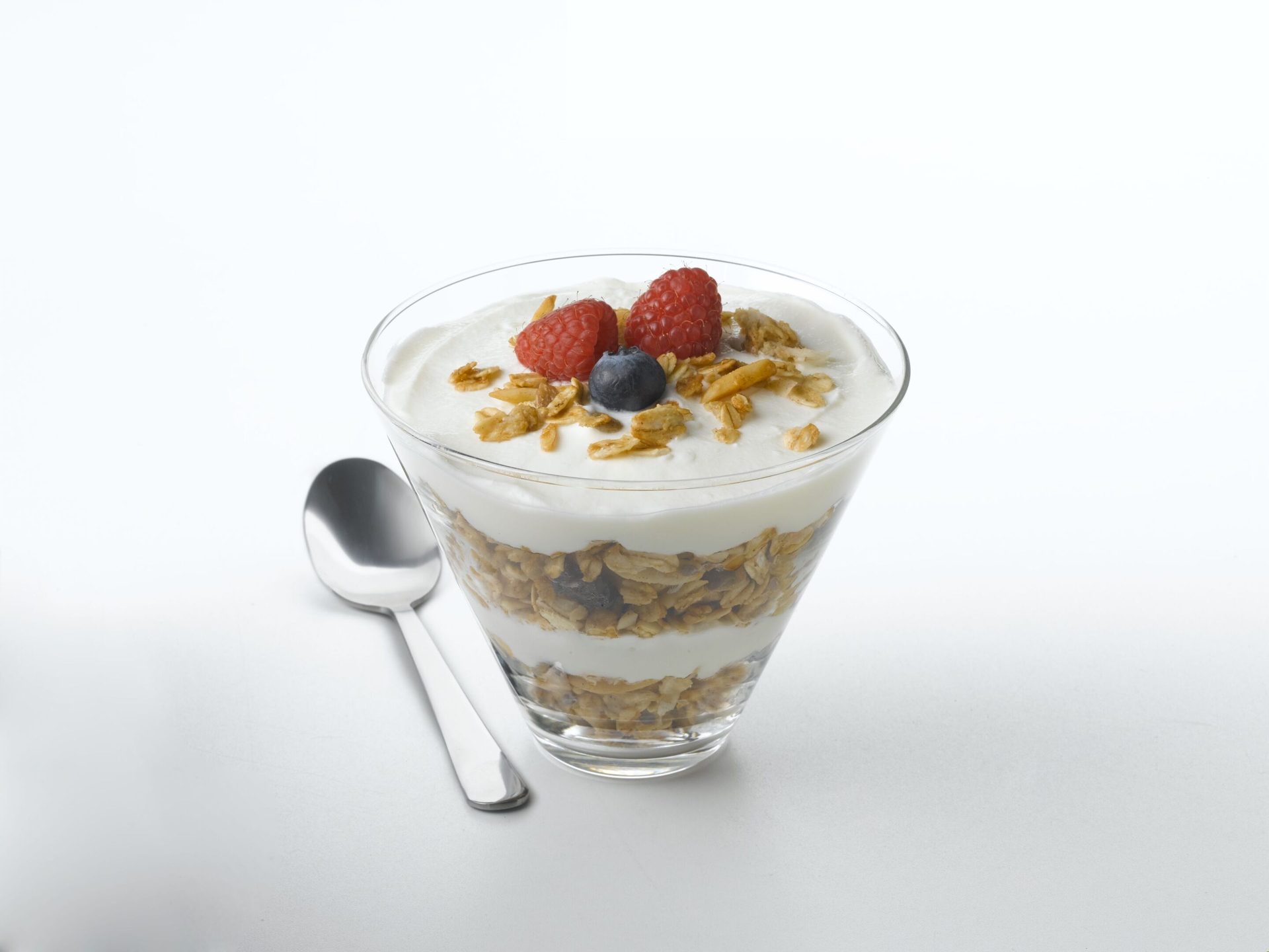 Yogurt parfait with layers of granola, yogurt, and topped with raspberries, blueberries, and granola.