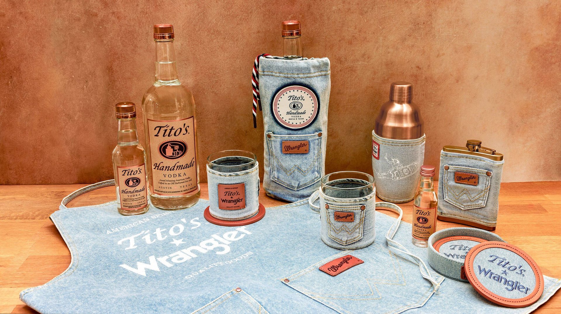 Tito's Vodka bottles with denim-themed accessories like glasses, shaker, flask, and apron from a collaboration.