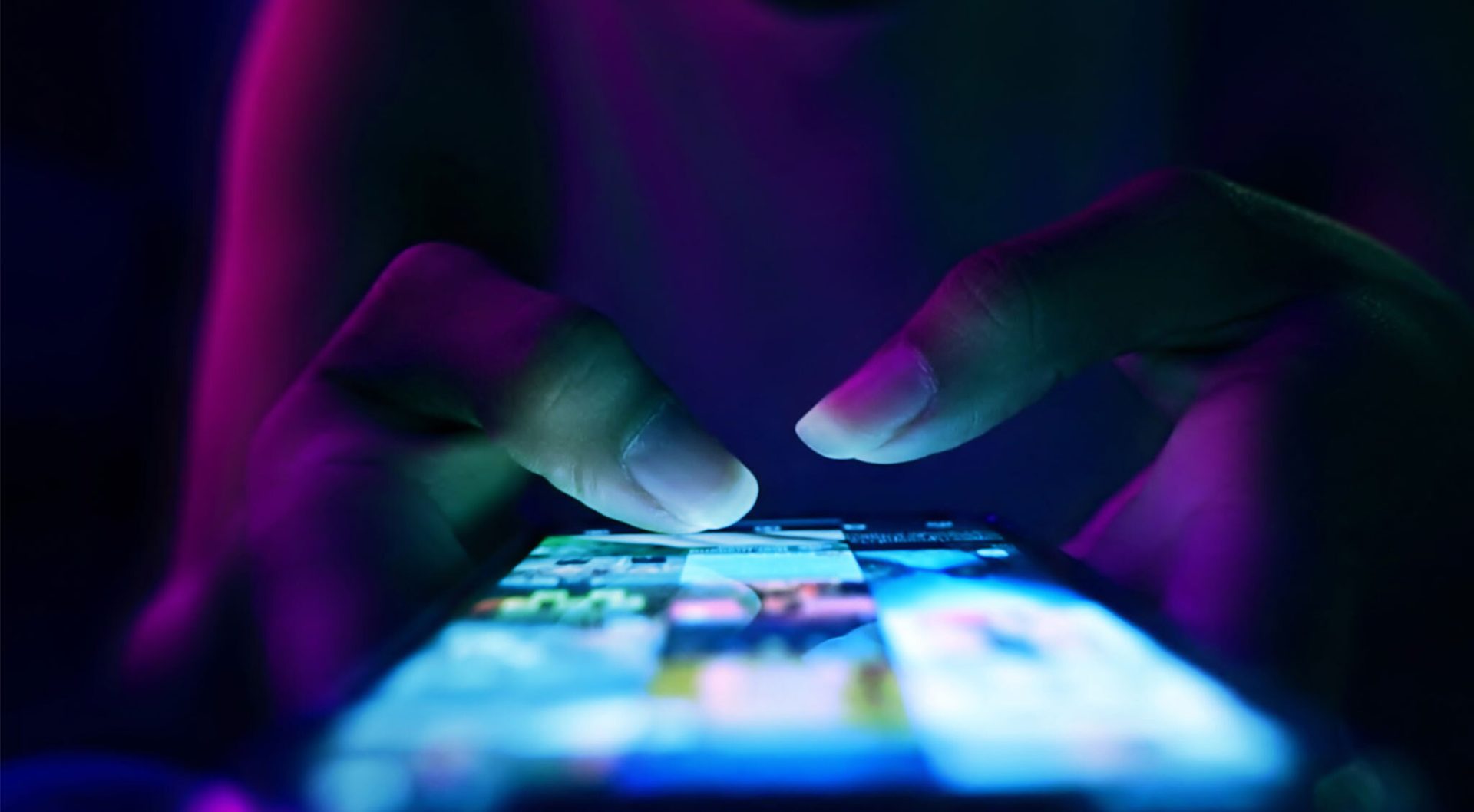 Hands using a glowing smartphone screen in neon light.