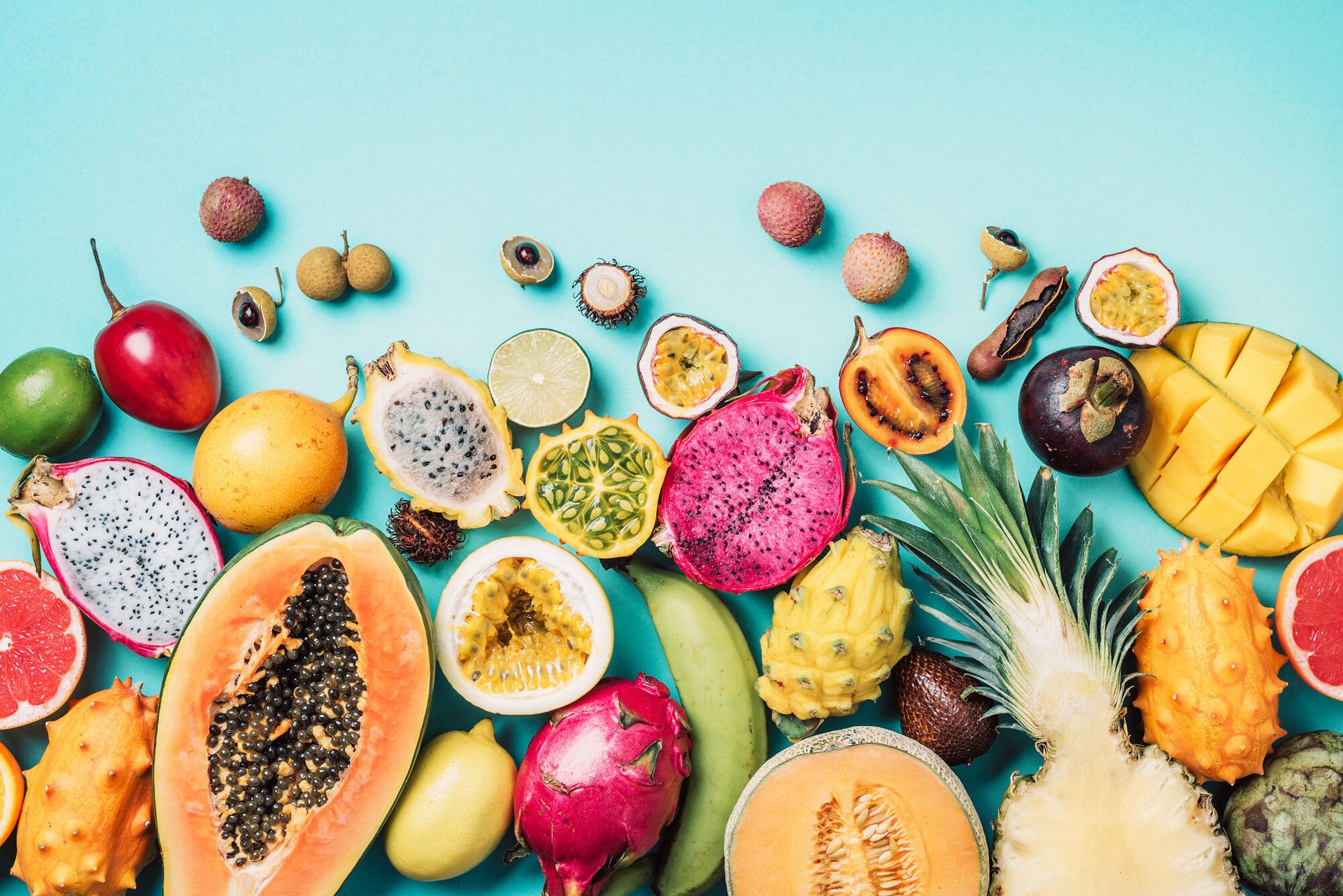 Vibrant, diverse exotic fruits, some sliced, on a blue background.