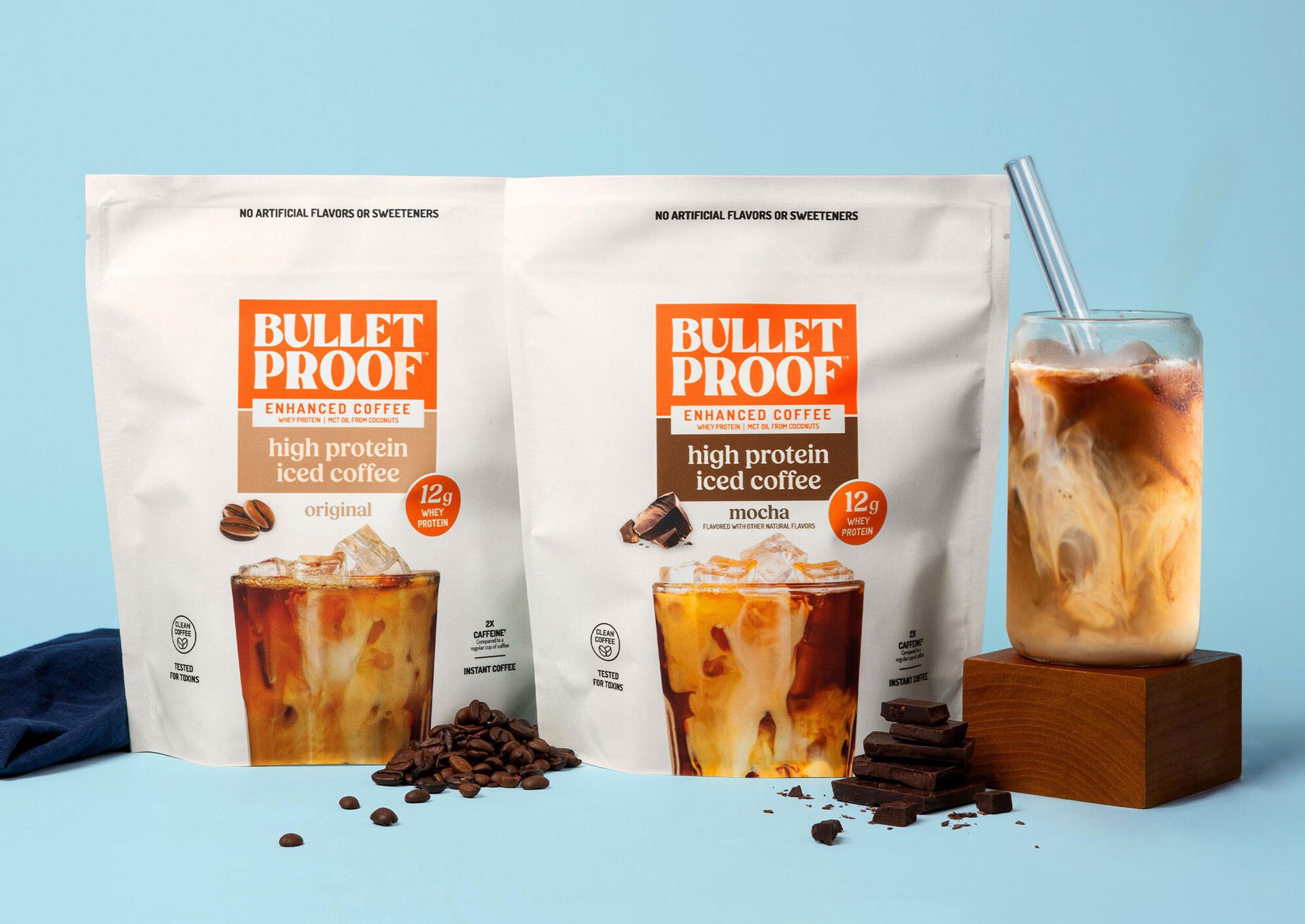 Two Bulletproof high protein iced coffee bags (Original & Mocha) with a glass of iced coffee.