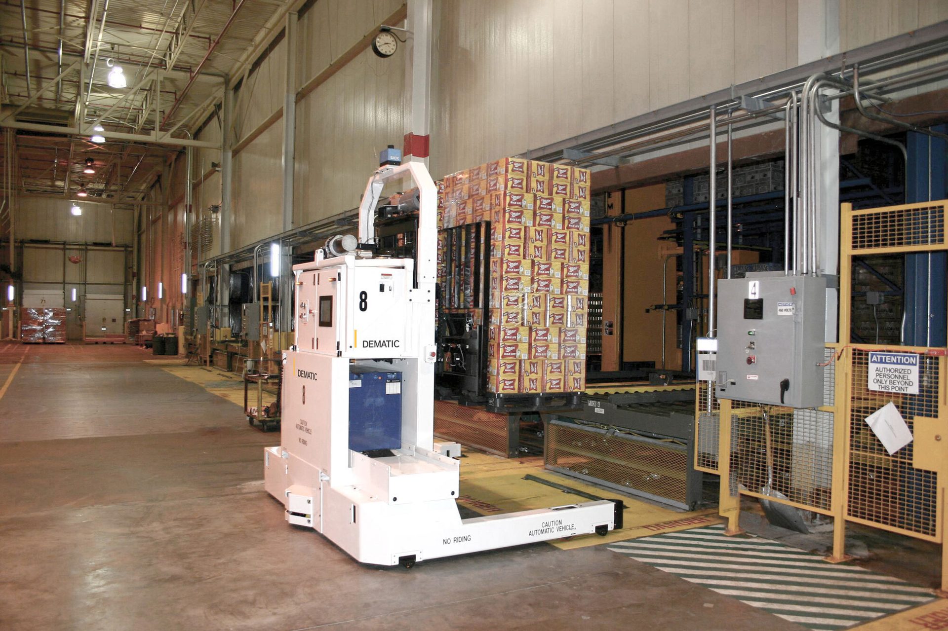 A DEMATIC automatic vehicle in a large warehouse, next to stacked boxes of products.
