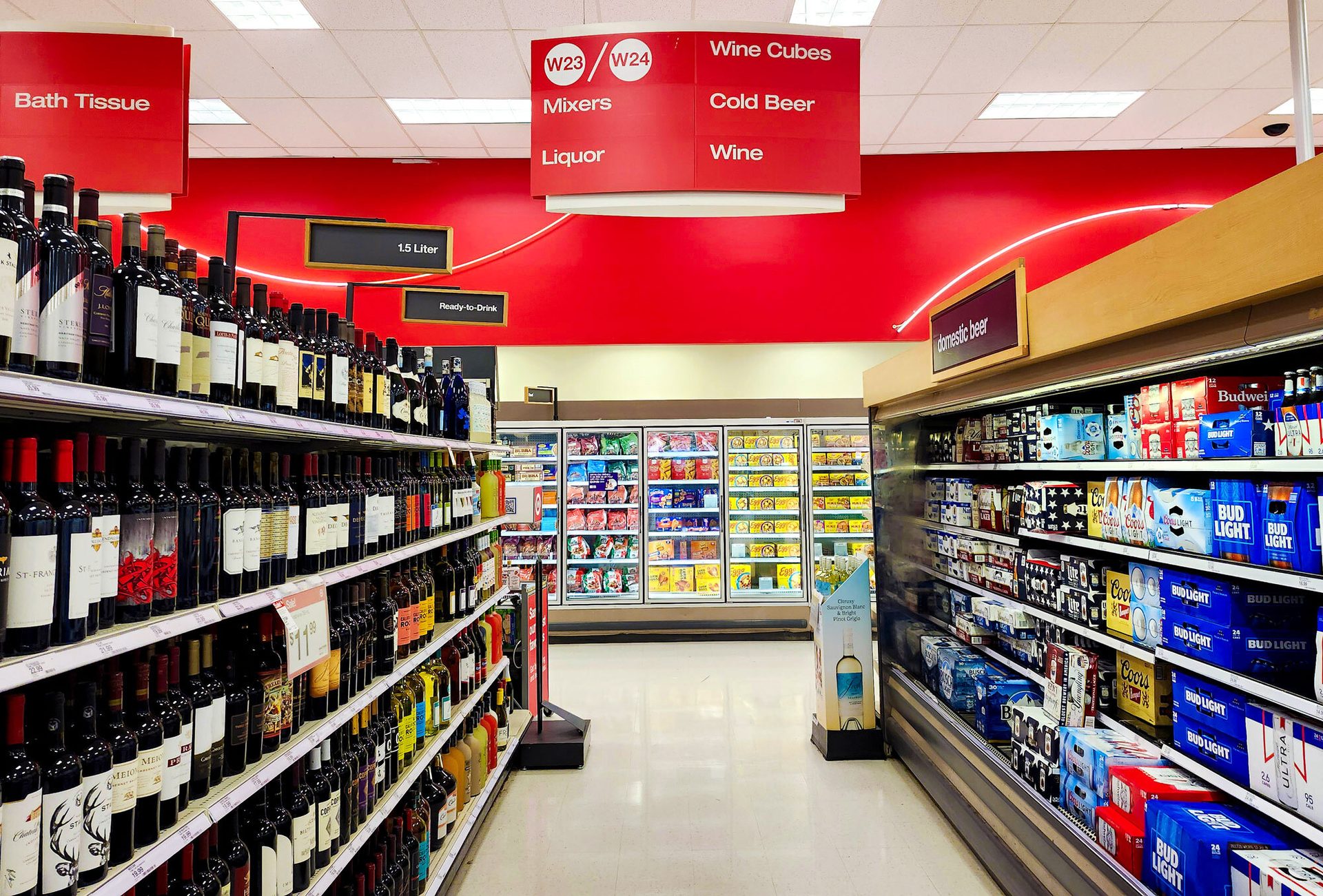 Store aisle with wine bottles, cold beer, and freezers. Overhead signs for Wine, Liquor, and Beer.