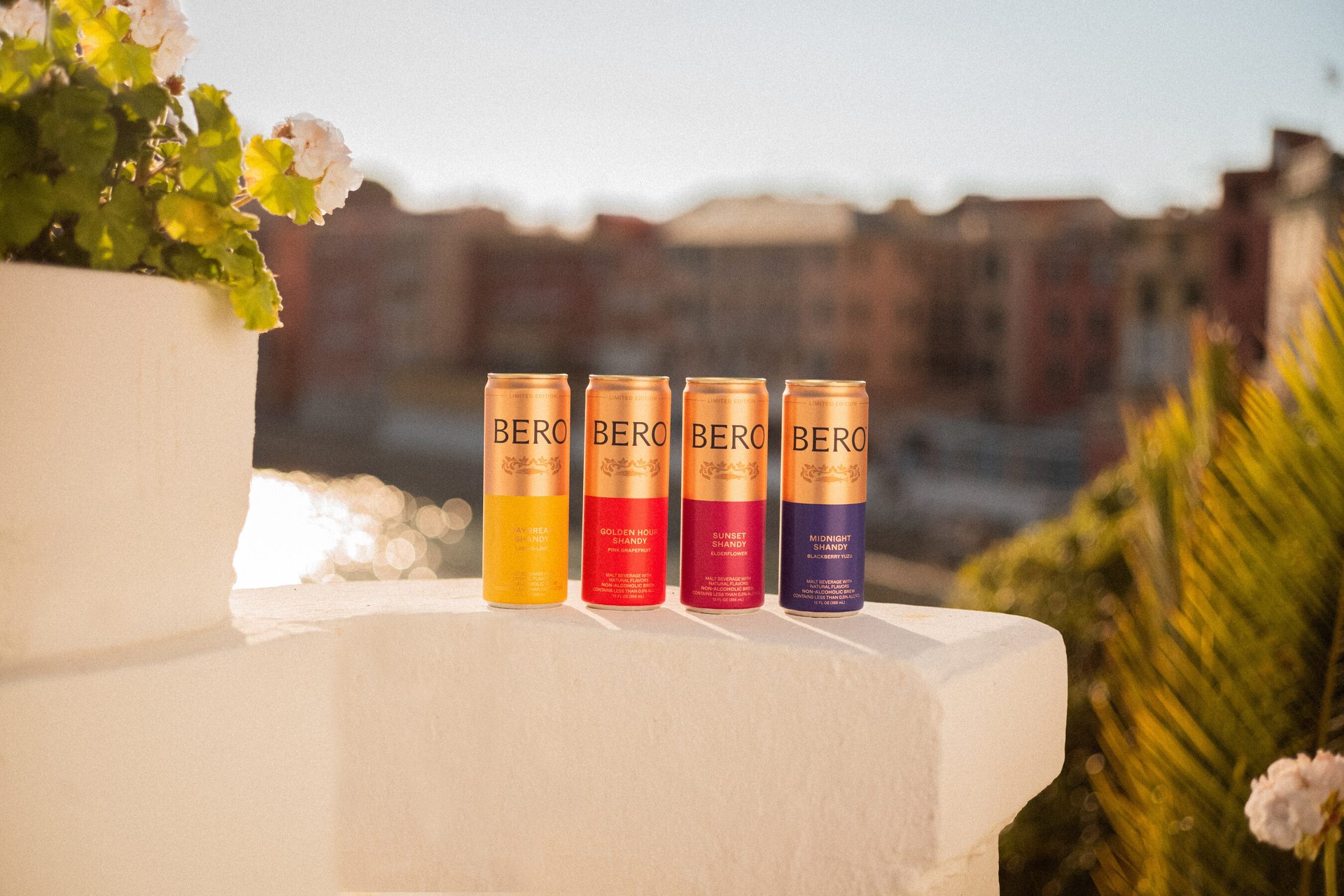 Four colorful BERO beverage cans lined up on a white wall overlooking a blurred city and water background.