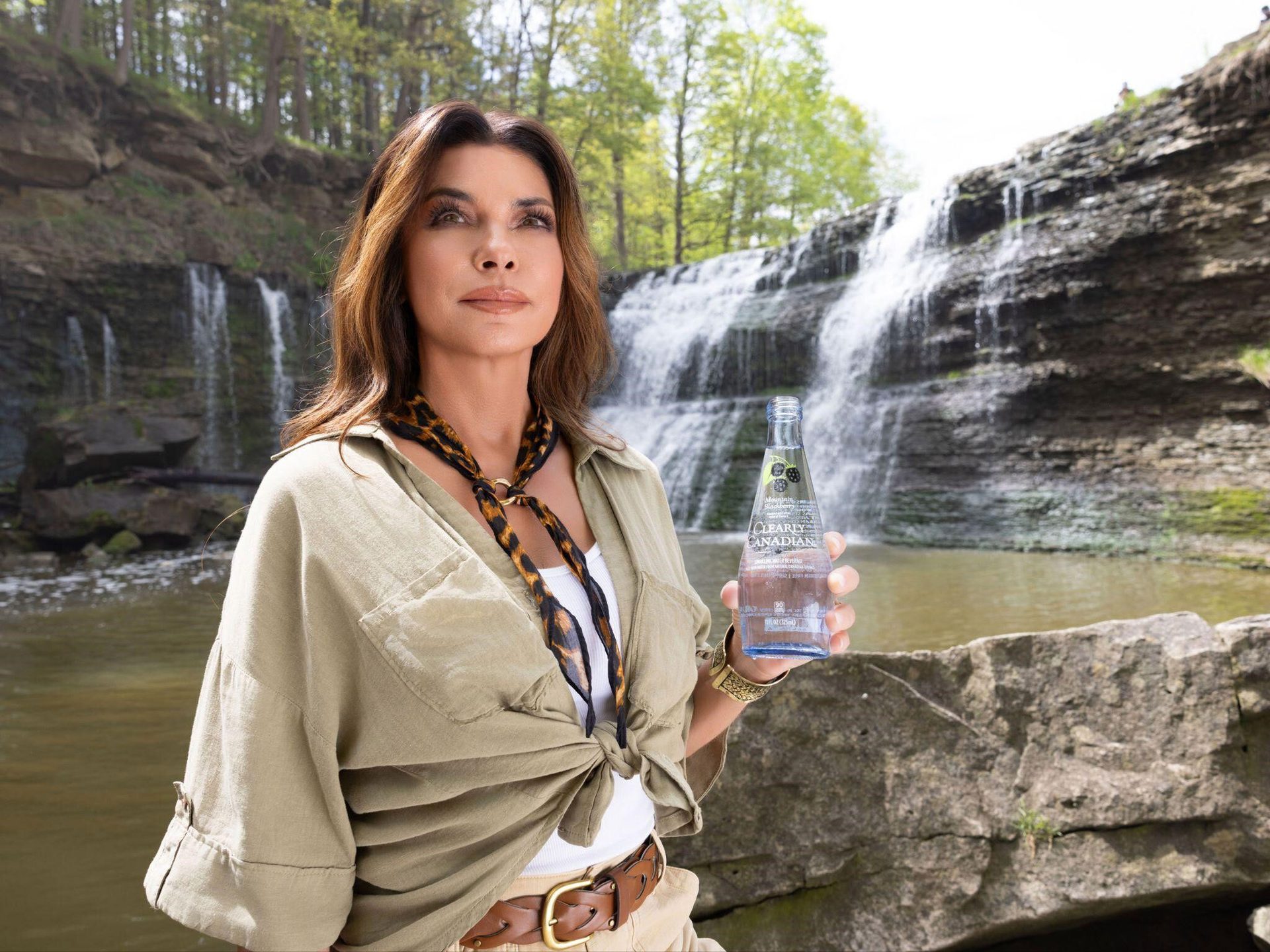 A woman holds a Clearly Canadian bottle at a waterfall.