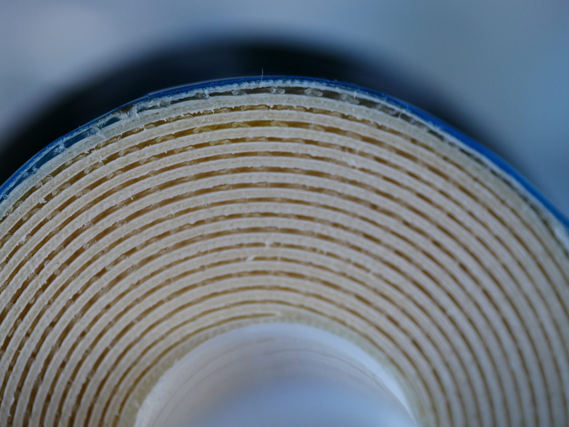 Close-up of a rolled material's cross-section, showing numerous beige layers beneath a blue top layer.