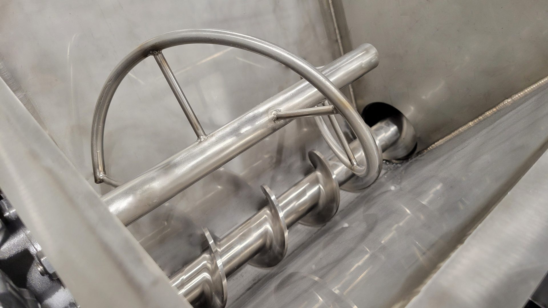 Industrial stainless steel mixer interior with helical auger and stirrer.