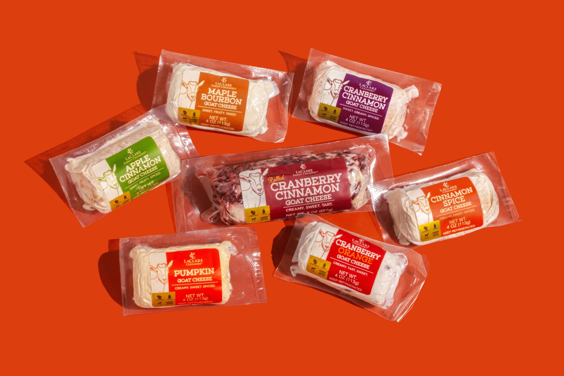Assorted flavored LaClare goat cheeses, including Maple Bourbon and Cranberry, on an orange background.