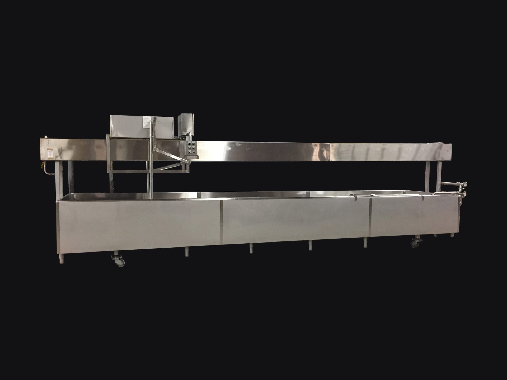 Long stainless steel industrial processing or conveying machine with an upper rail and lower trough.