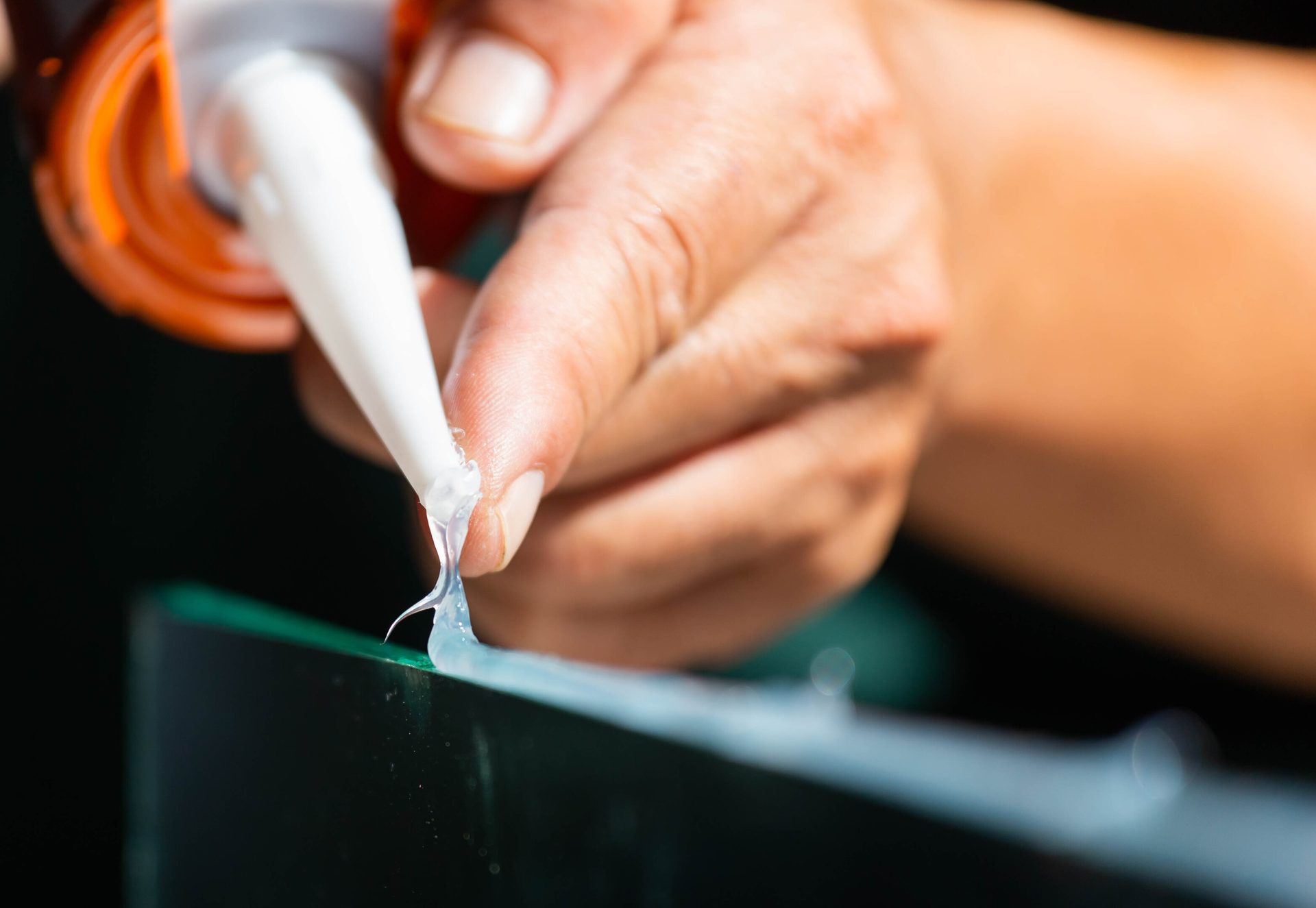 Hand applying transparent sealant from a tube onto a surface.