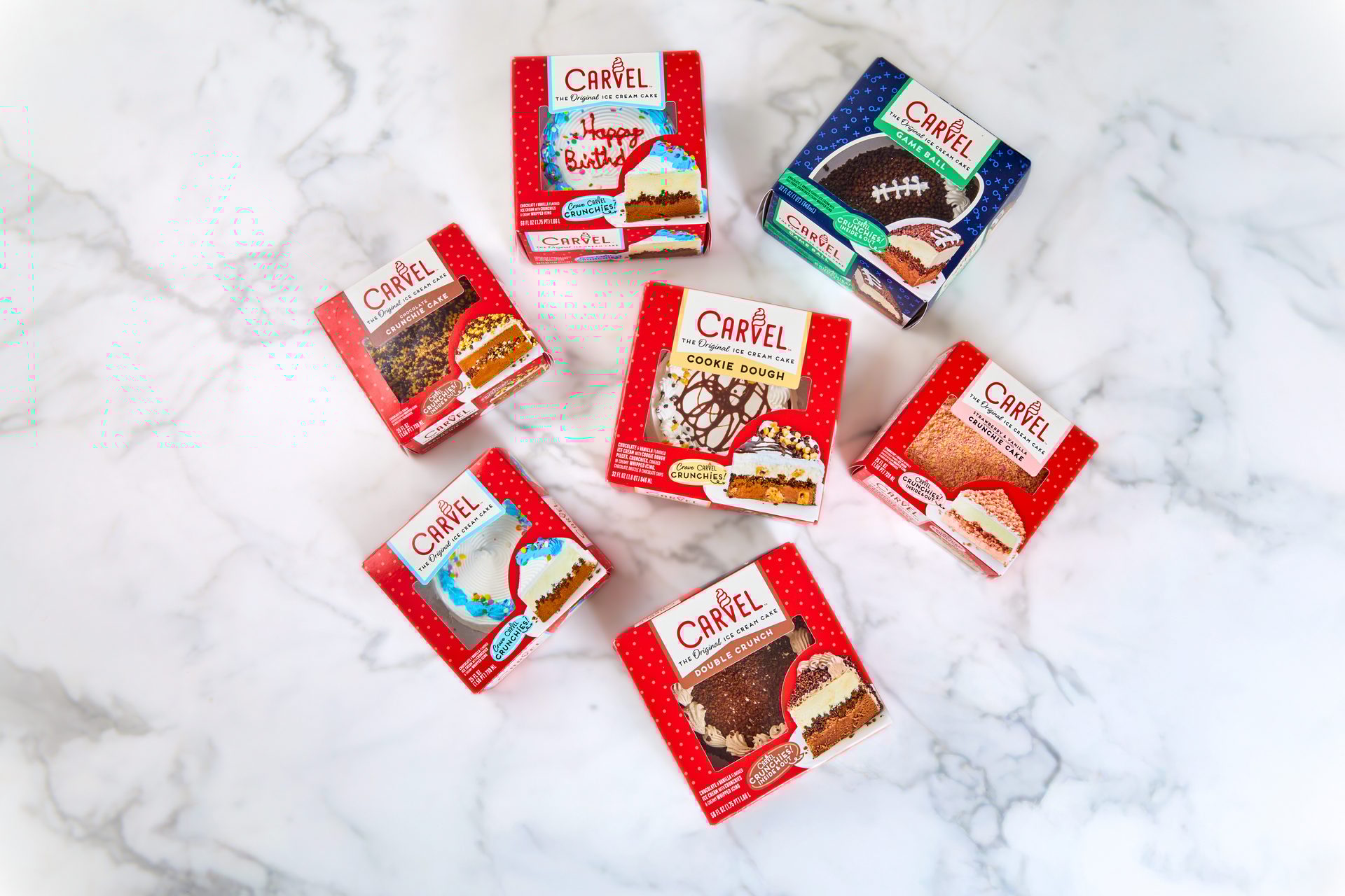 Six Carvel ice cream cake boxes on a marble surface, featuring Birthday, Cookie Dough, Game Ball, and Crunchie flavors.