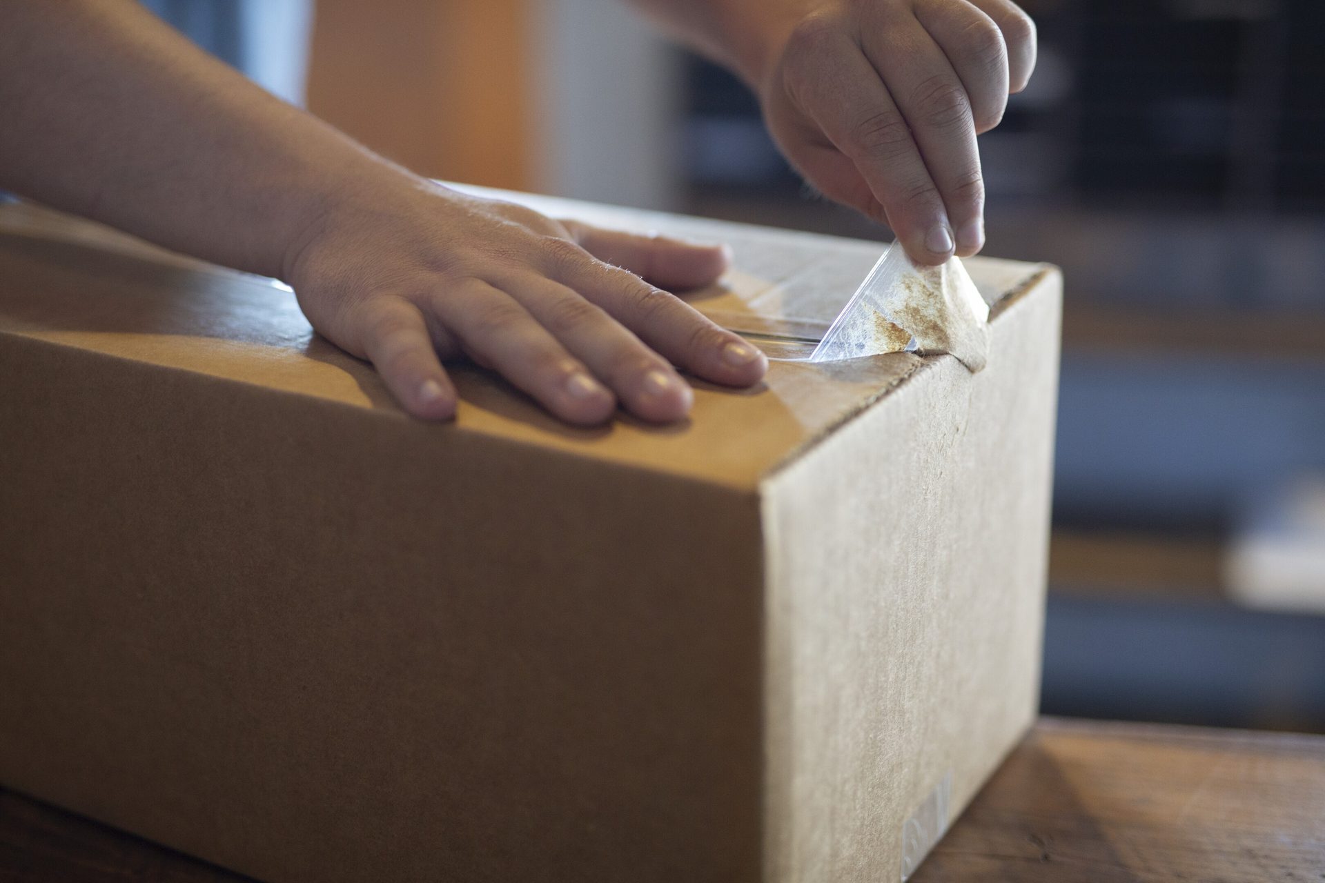 Hands unsealing a cardboard box by pulling tape.