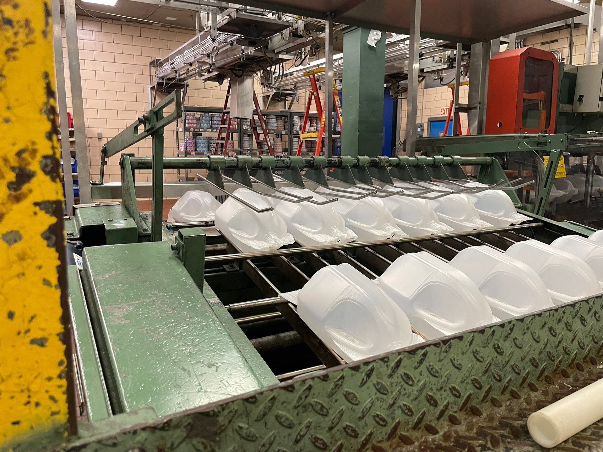 Empty white plastic milk jugs moving along a green conveyor belt in a dairy factory.