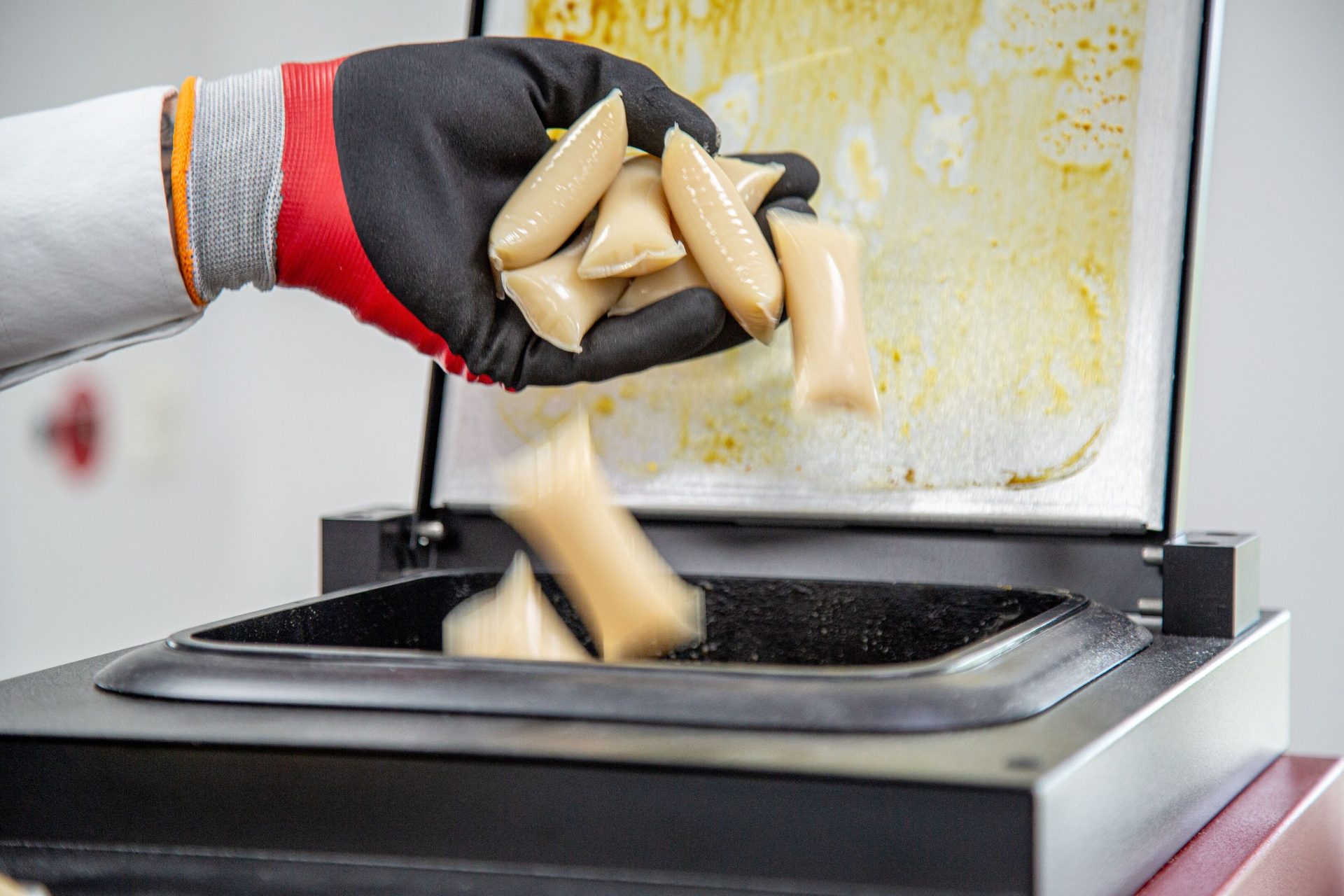 Gloved hand dropping small, light-colored pouches into a machine's open compartment.