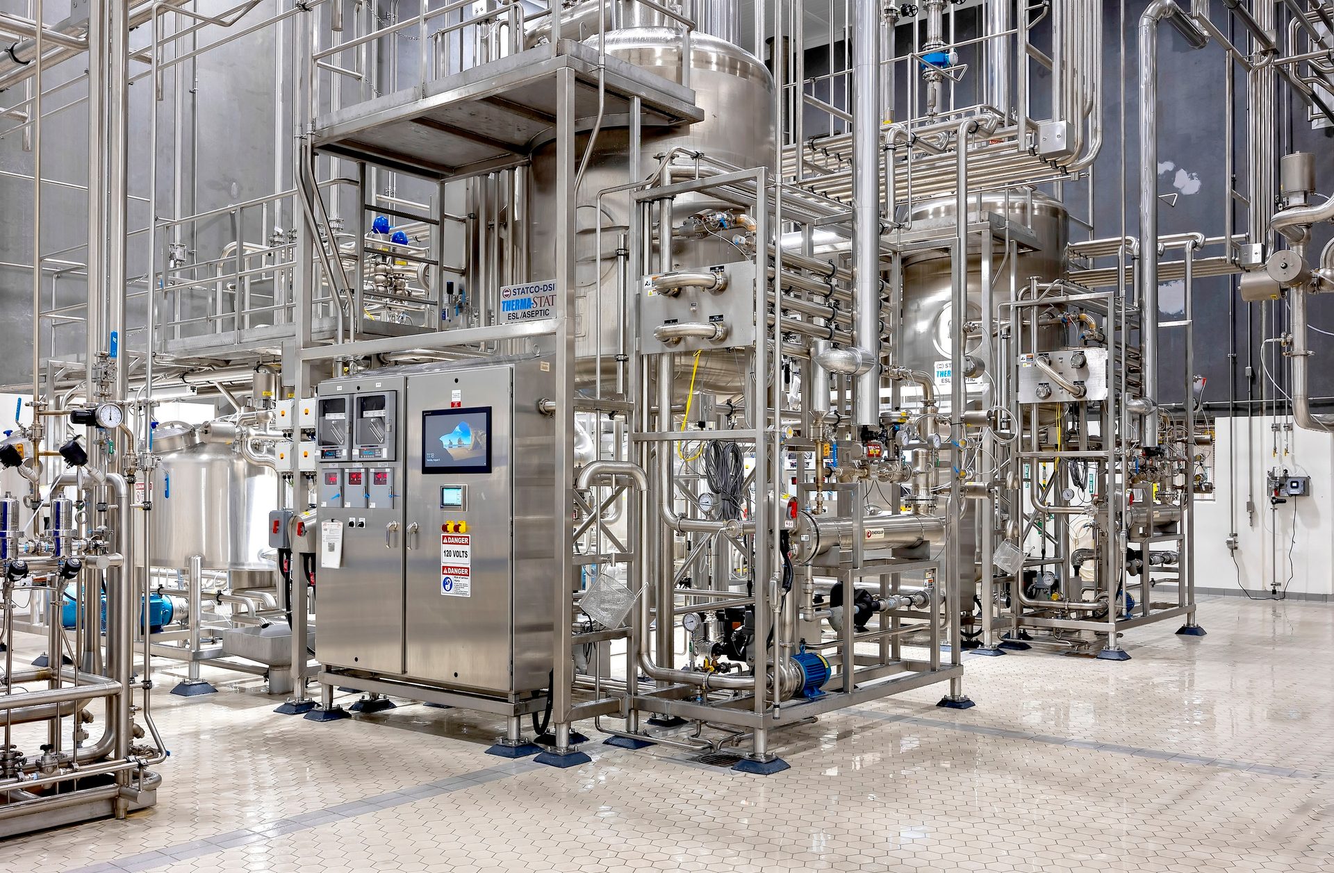 Stainless steel industrial processing equipment with pipes, tanks, and control panels in a clean room.