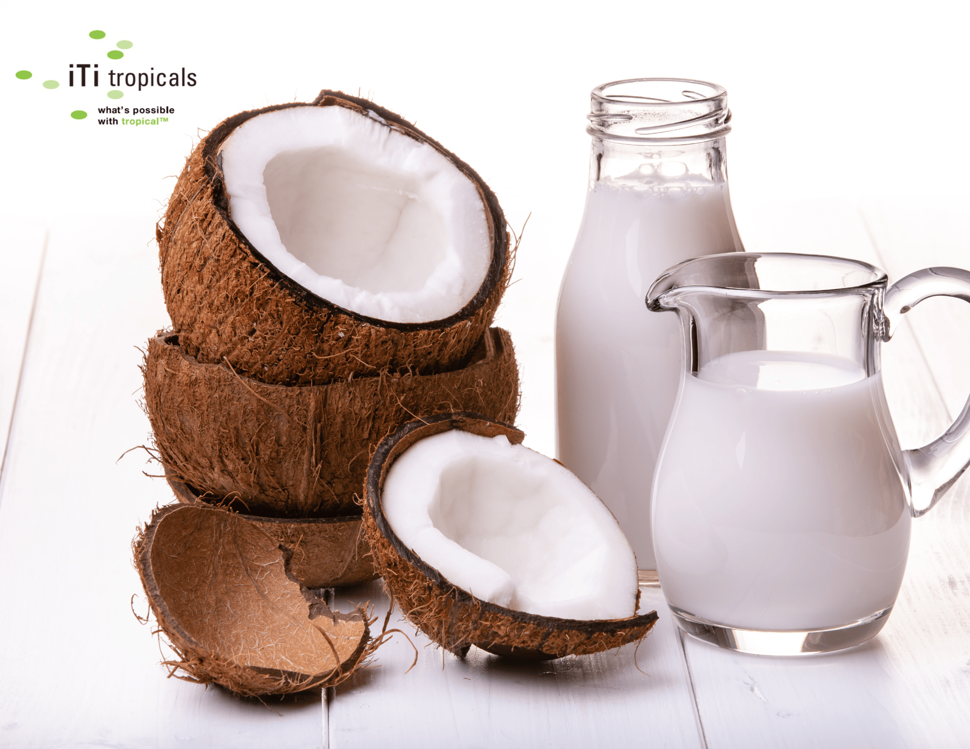iTi tropicals logo, cracked coconuts, and coconut milk in a bottle and pitcher on white wood.