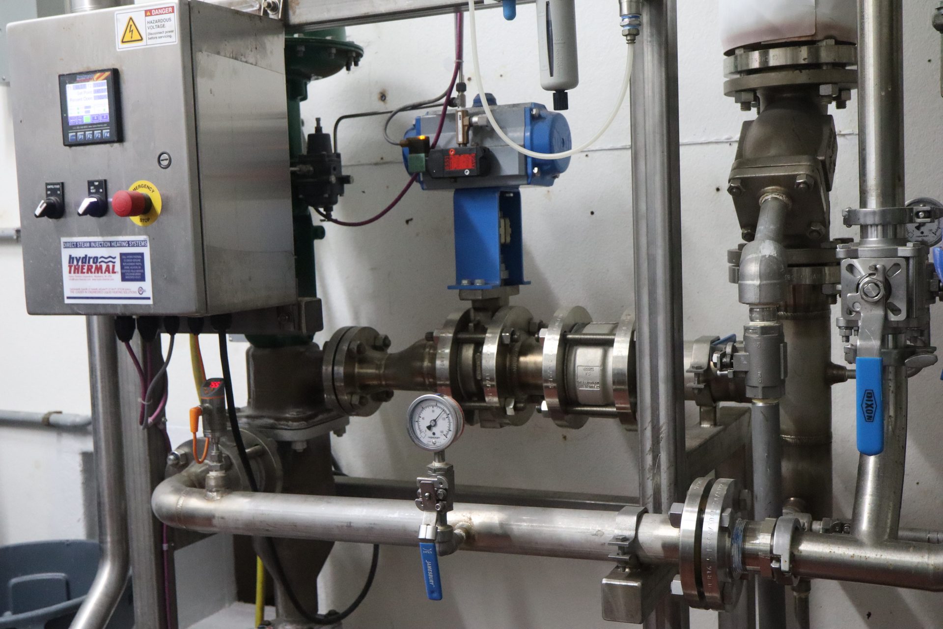 Industrial steam injection heating system with a control panel, stainless steel pipes, valves, and gauges.