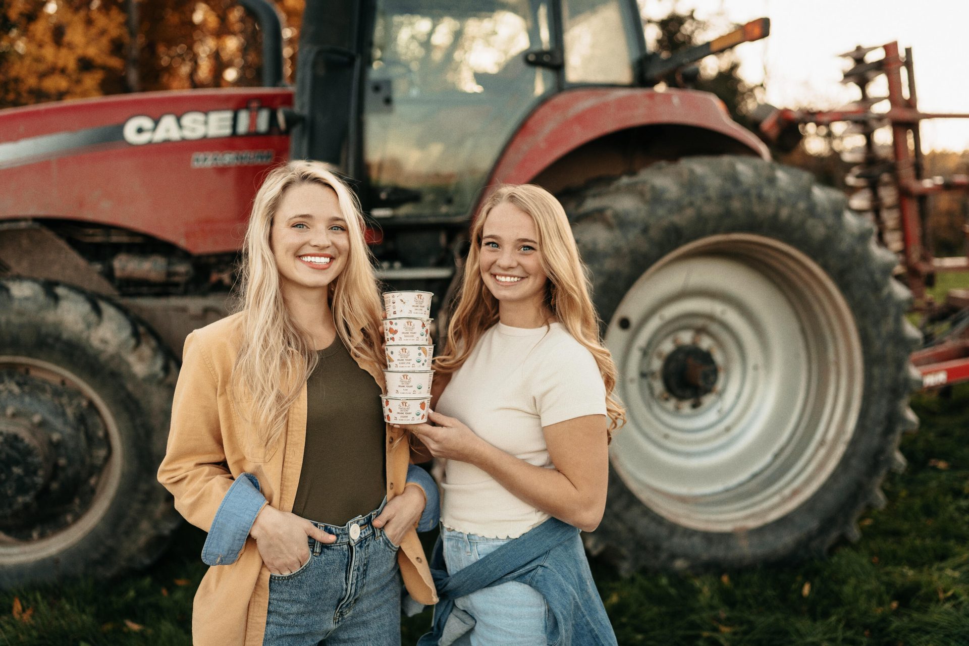 Smiling women with product cups pose in front of a red tractor on a farm.