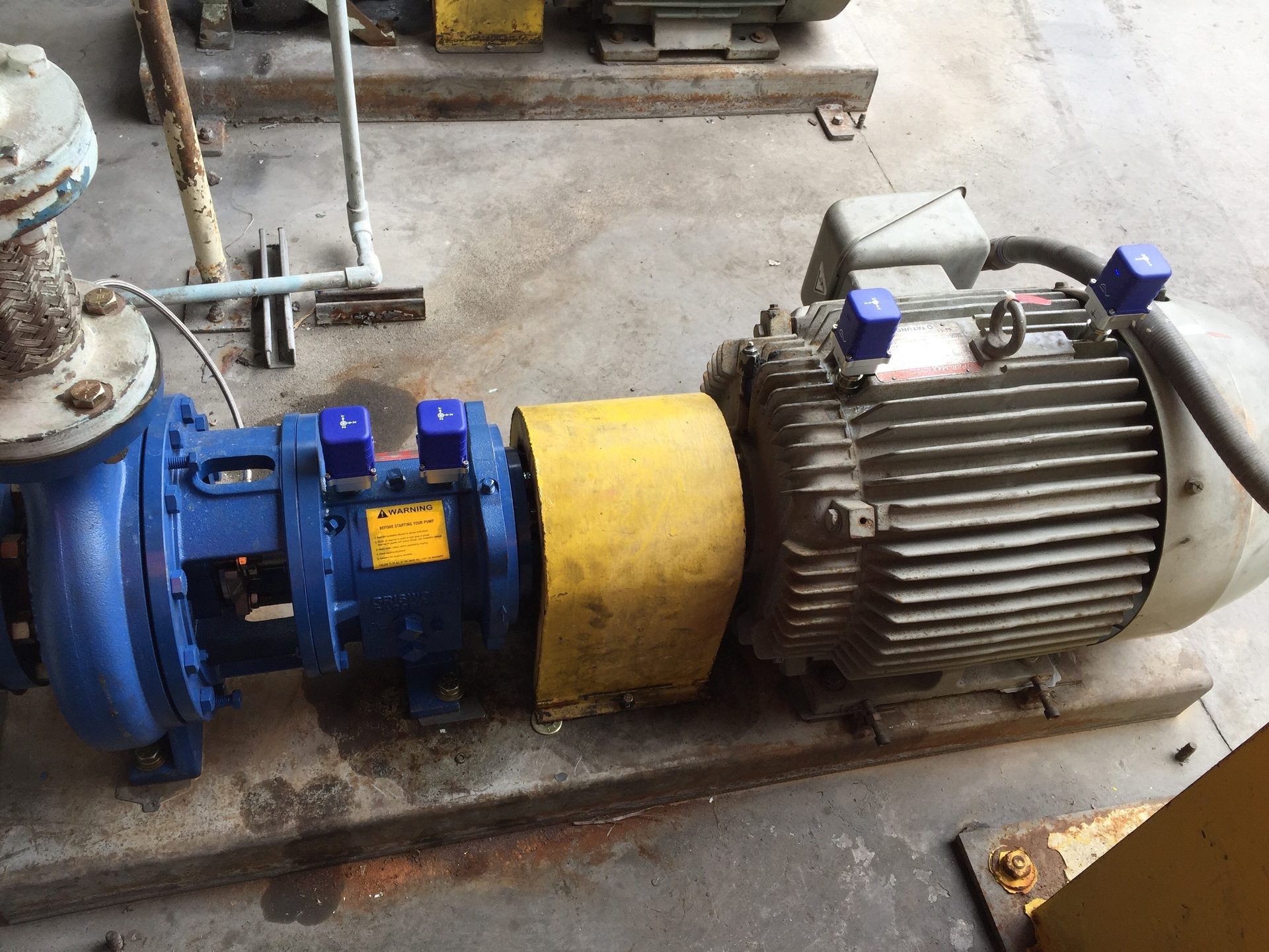 Blue industrial pump and gray electric motor with a yellow coupling guard and blue sensors.