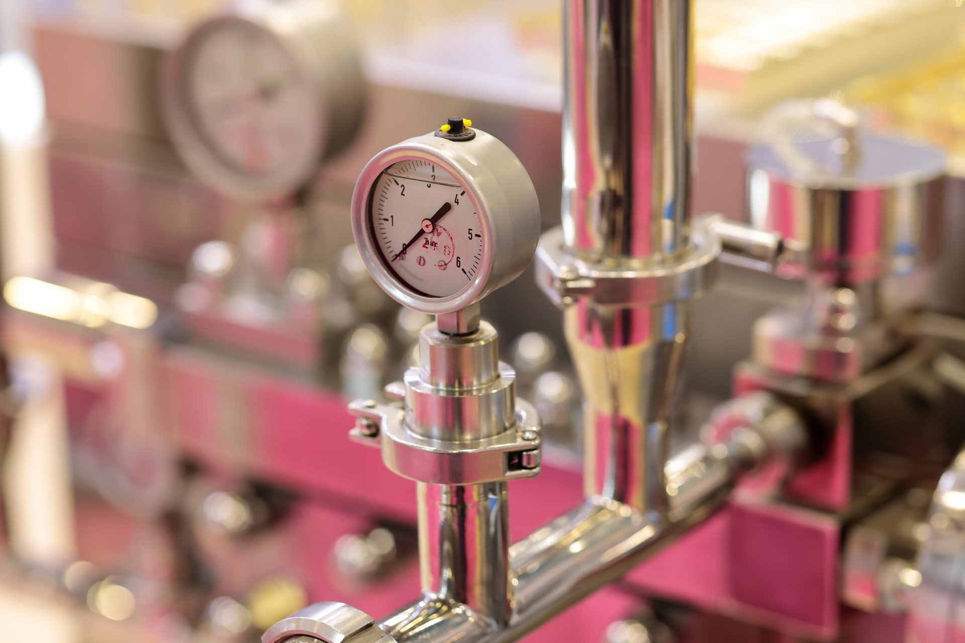 A close-up of a pressure gauge on shiny stainless steel industrial piping, showing current readings.
