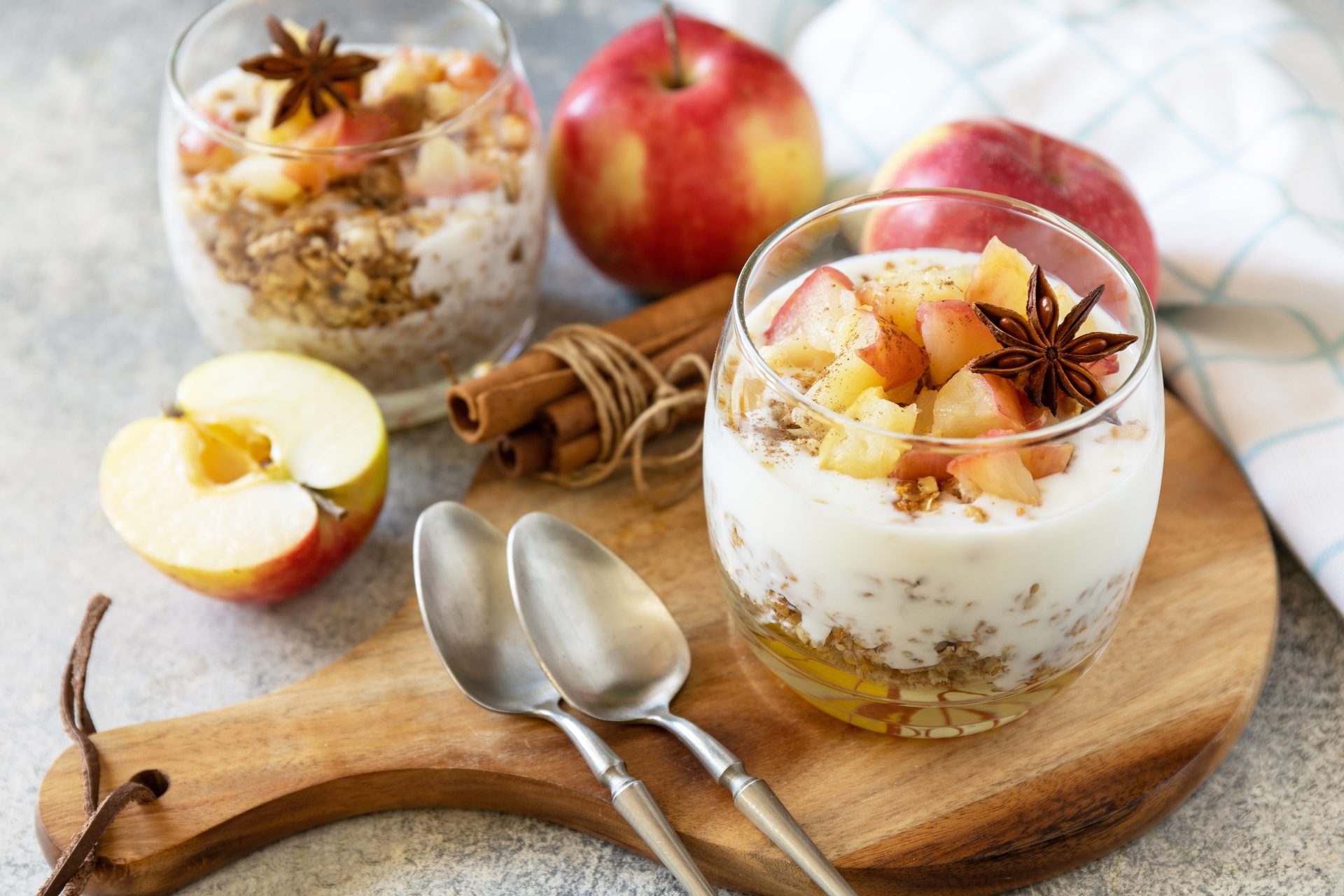Apple cinnamon yogurt parfaits with granola, star anise, and fresh apples on a wooden board.