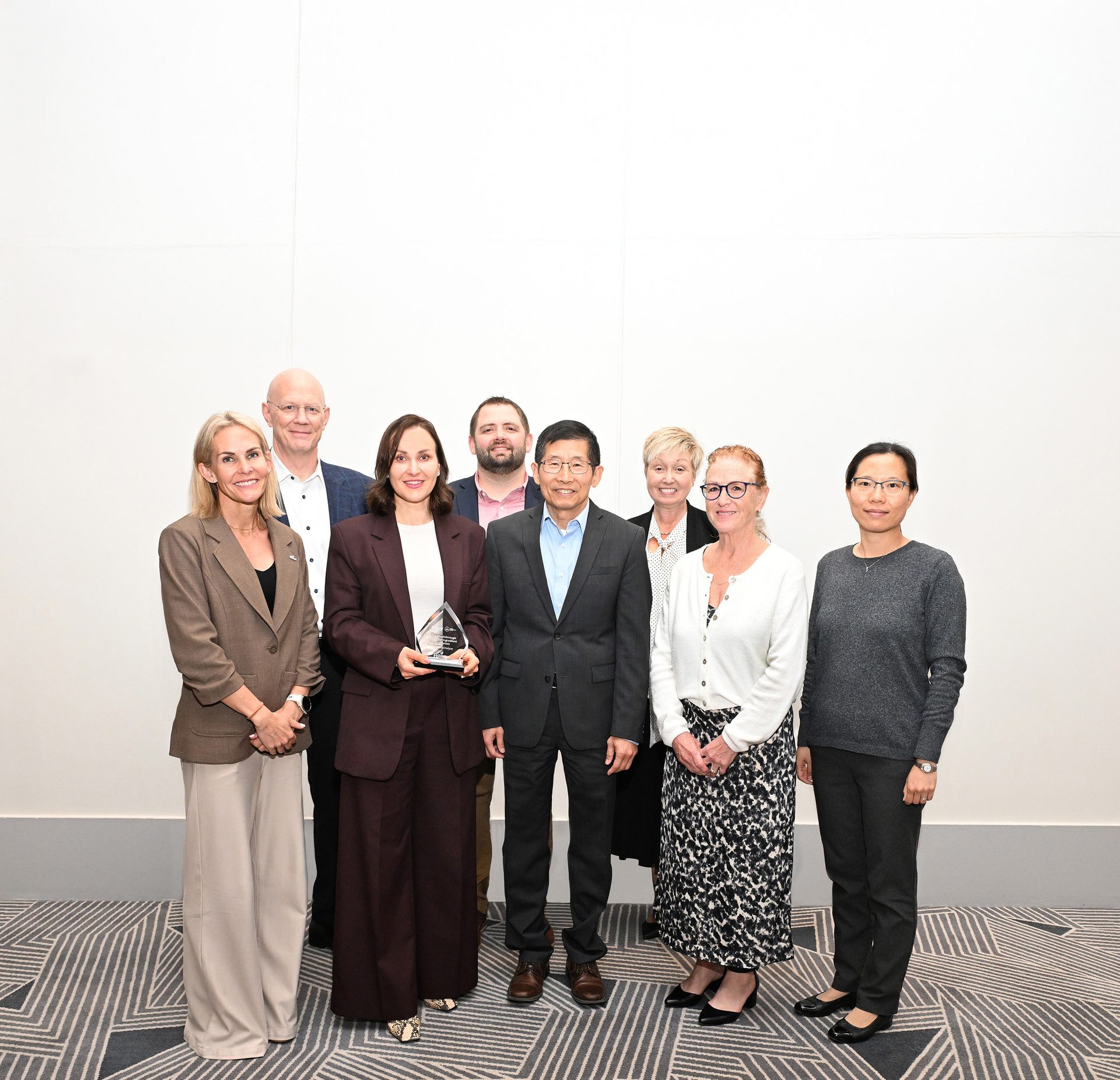 Nine professionals, one holding an award, pose for a group photo.