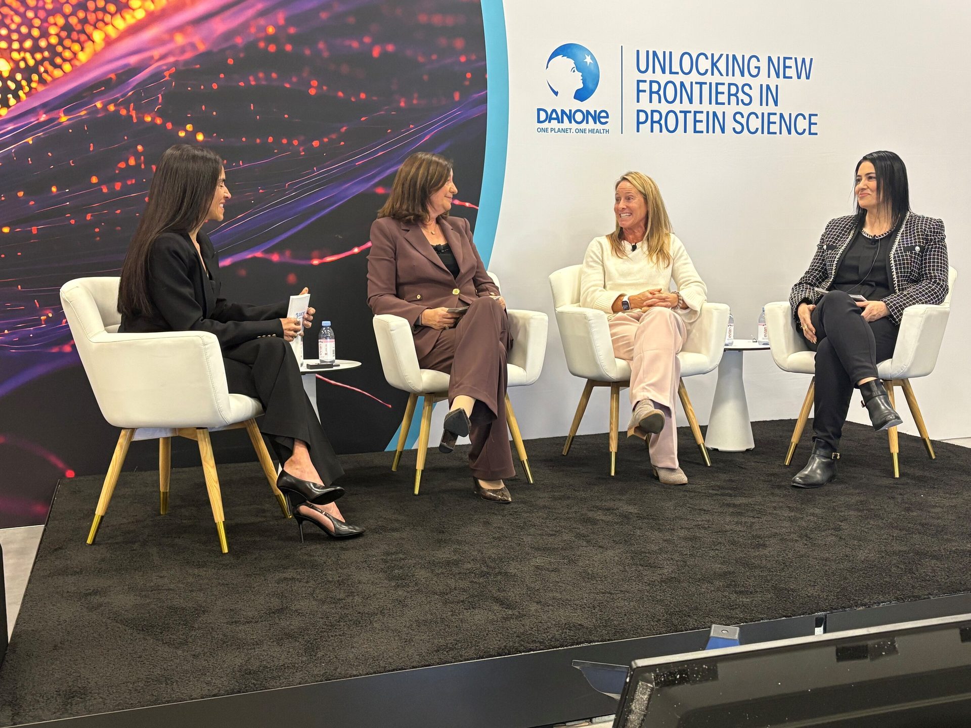 Four women on a panel discussing protein science, Danone branding visible.