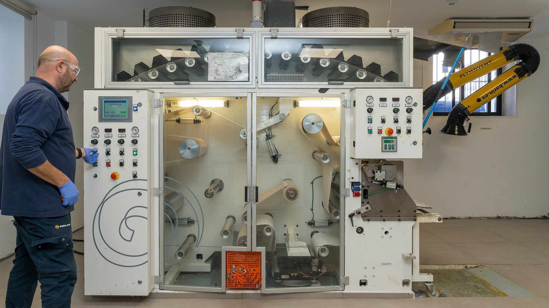 Man operating an industrial machine with a control panel and rolls of material.