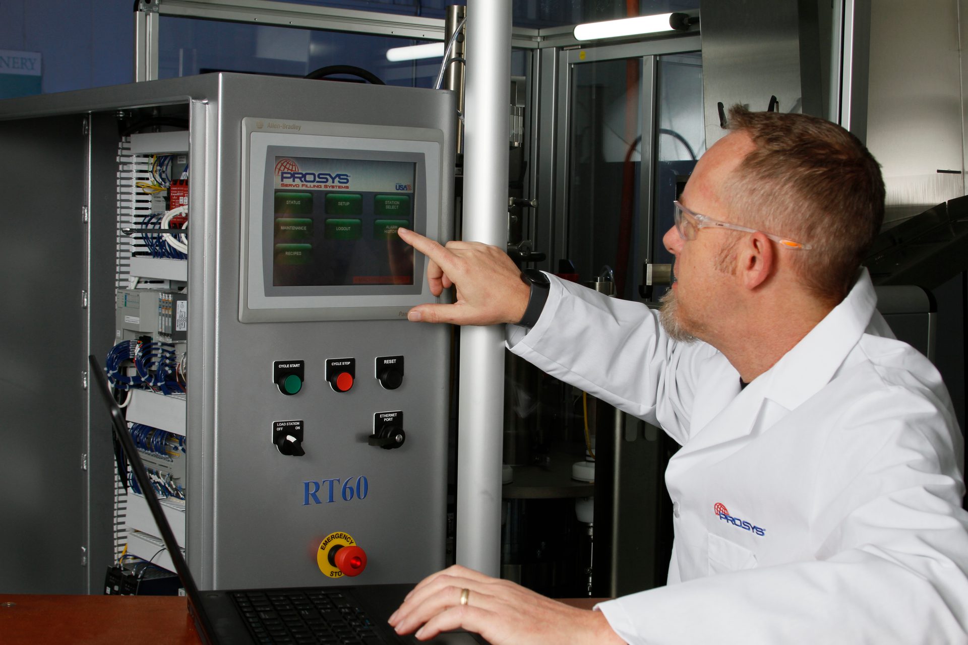 Engineer in safety glasses operates PROSYS RT60 servo filling system control panel with laptop.