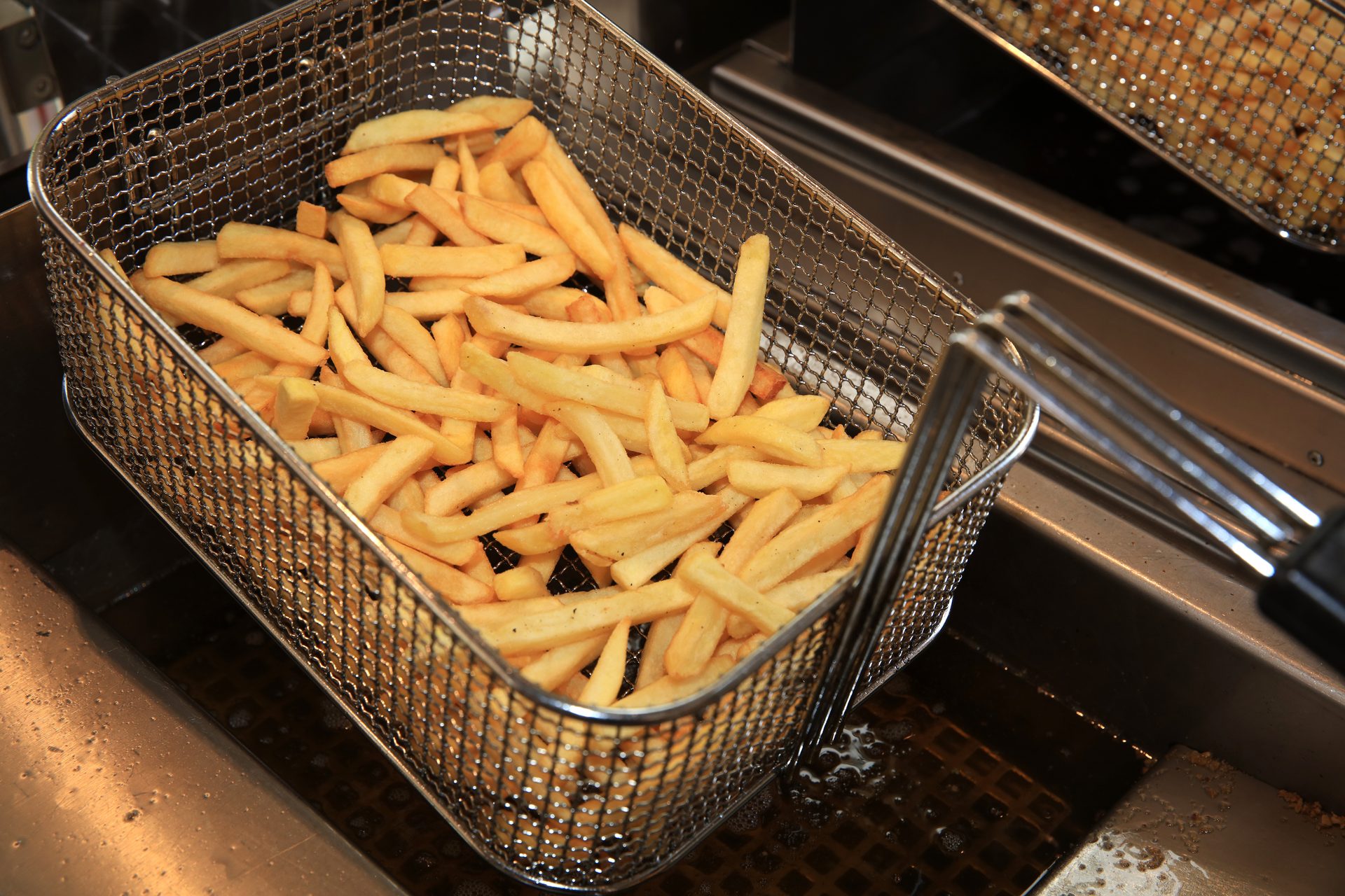 Golden french fries in a fryer basket, lifted from hot oil.