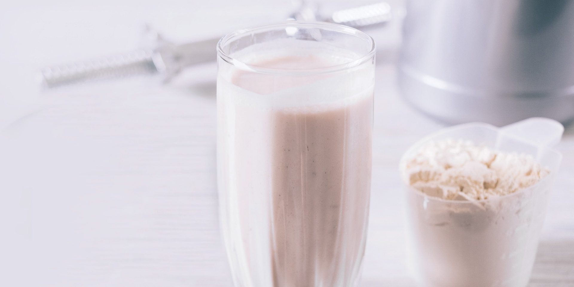Protein shake in glass, protein powder scoop, and blender.