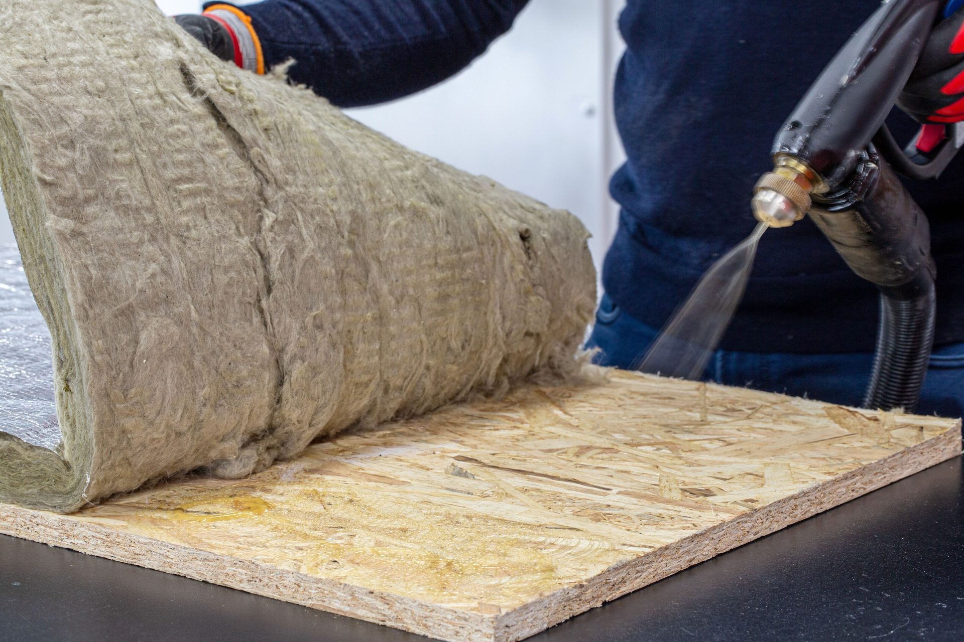 Spraying water onto a roll of mineral wool insulation on an OSB board.