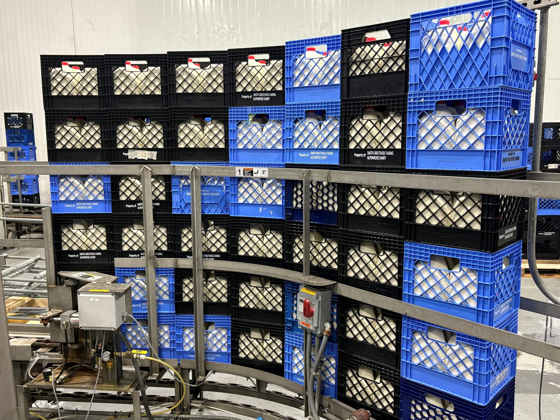 Stacks of Smith Brothers Farms milk crates, filled with jugs, on a curved conveyor system in a dairy.