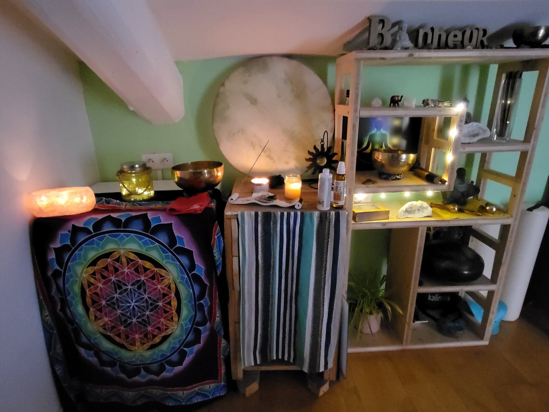 A spiritual altar with candles, singing bowls, a mandala tapestry, a drum, and a wooden shelf.