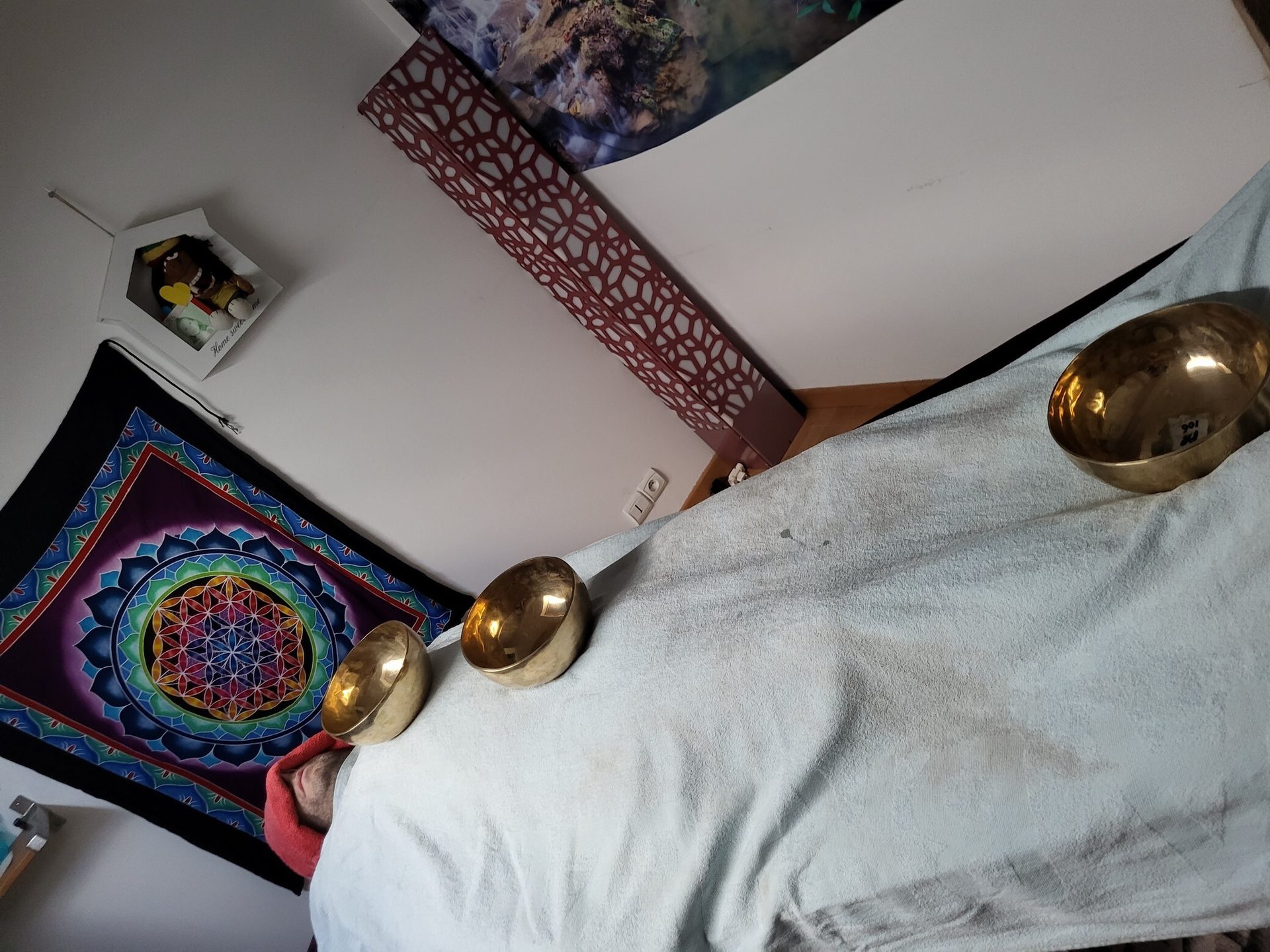 Three golden singing bowls on a bed with a colorful mandala tapestry and decorative panels in a room.