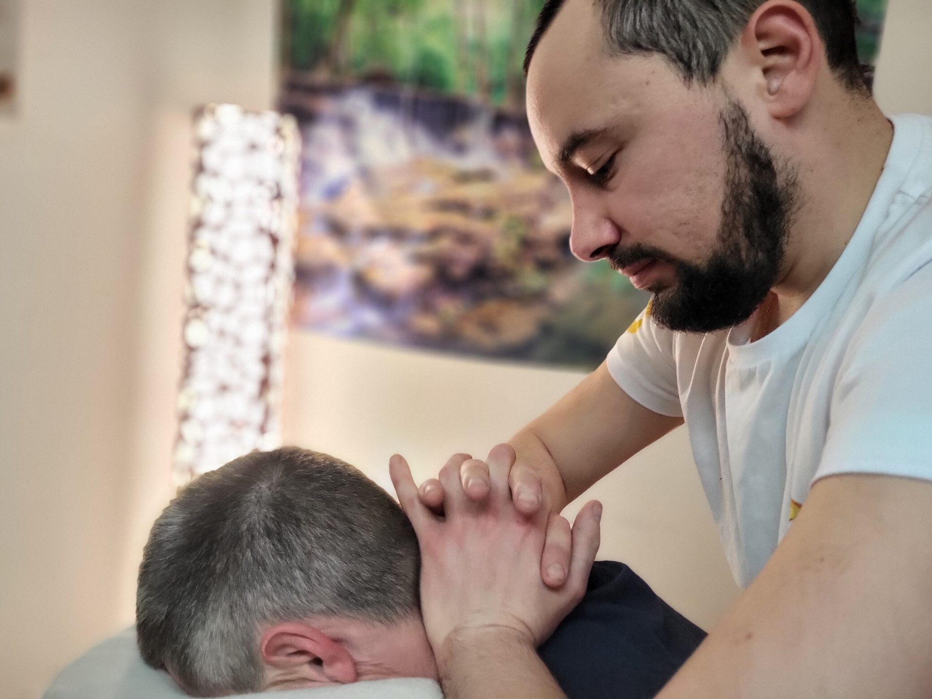 A bearded man massages another person's neck and upper back.
