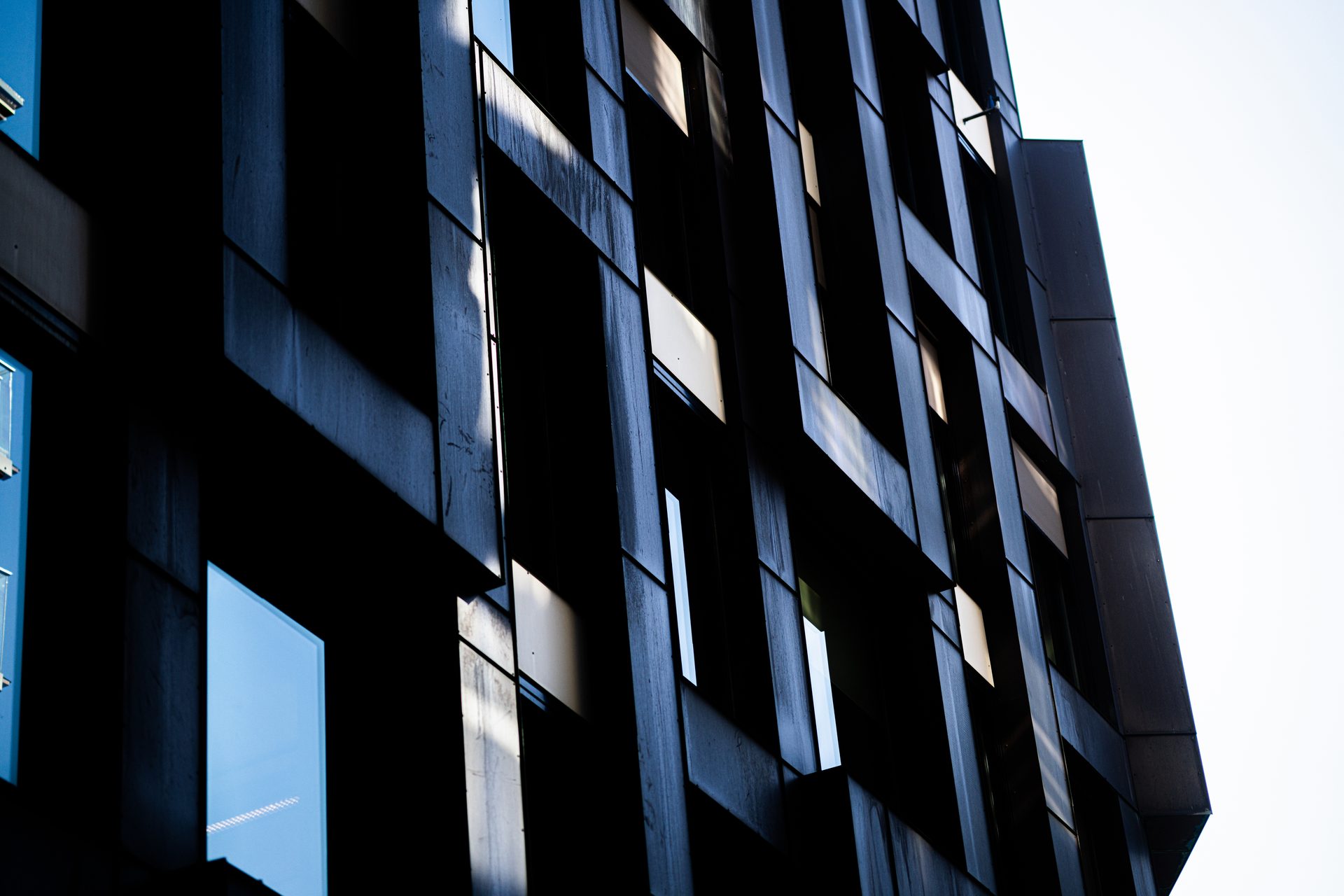 Abstract, low-angle view of a dark geometric building facade with reflective windows.