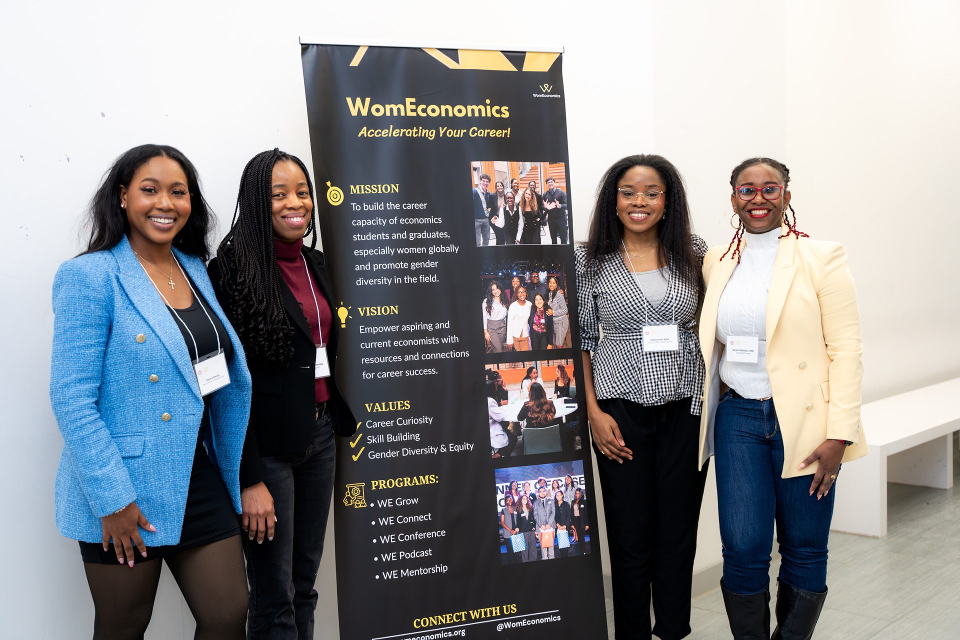 Four smiling women stand beside a WomEconomics banner, promoting career development and gender diversity.