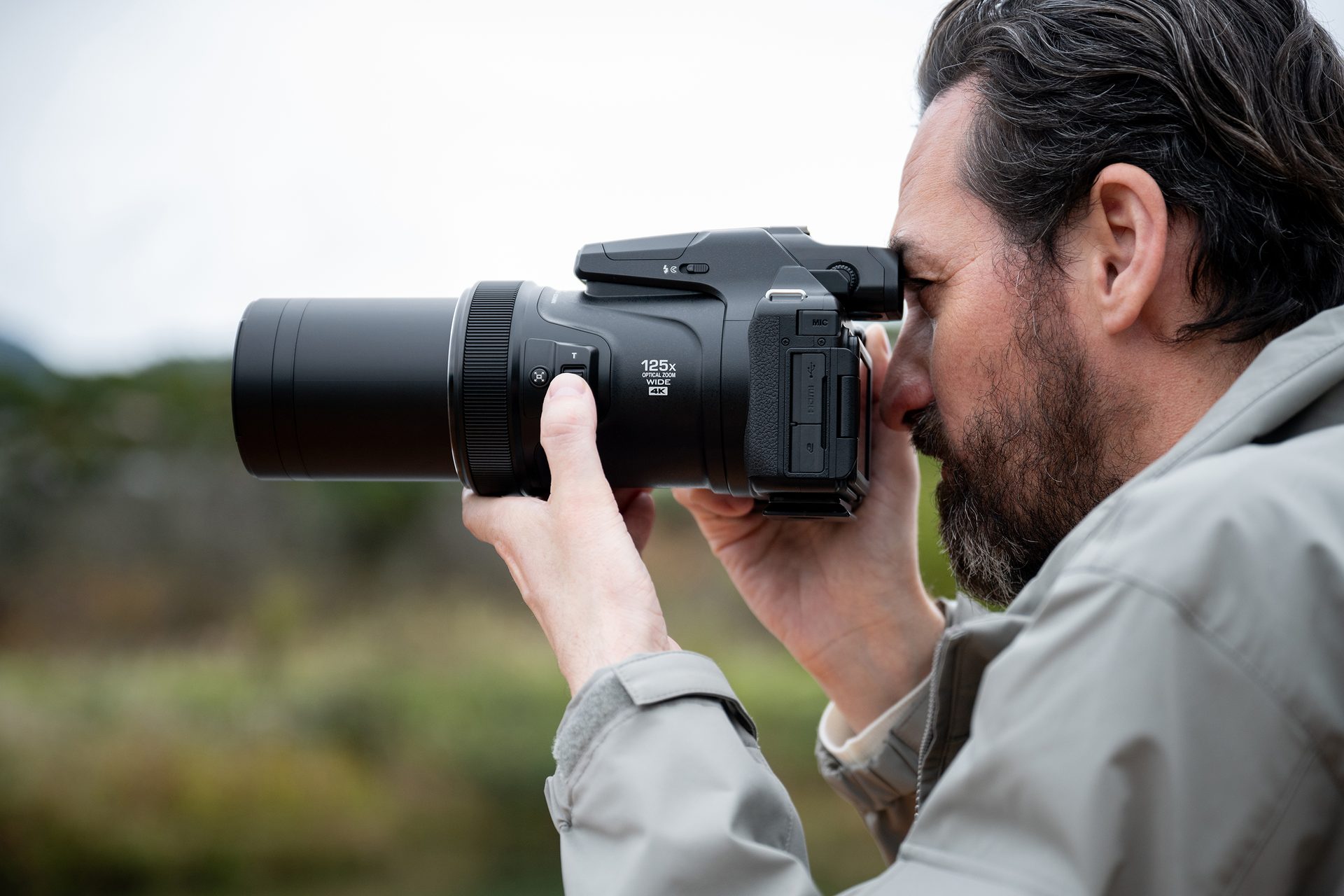 Man looking through a camera with a long zoom lens outdoors.