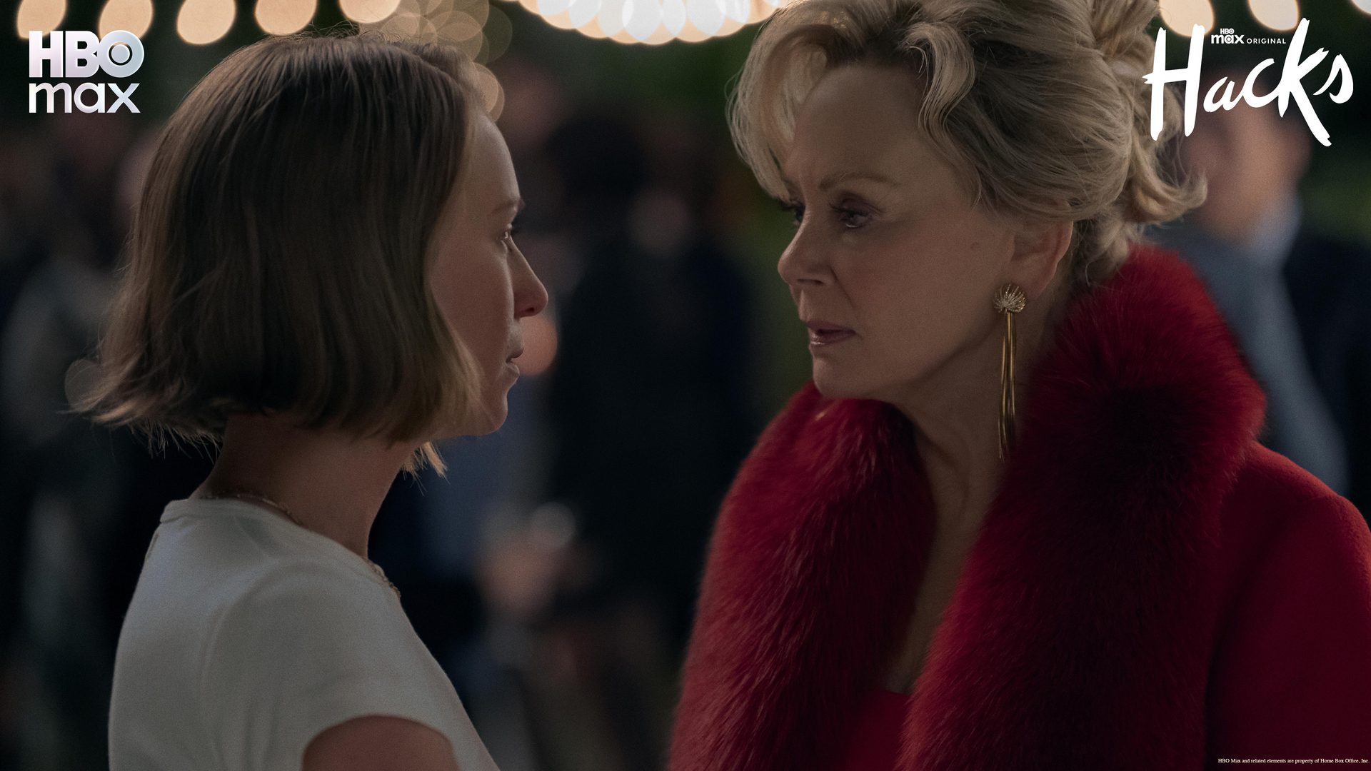 Two women, one in red fur, face each other intently. HBO Max "Hacks" promo.