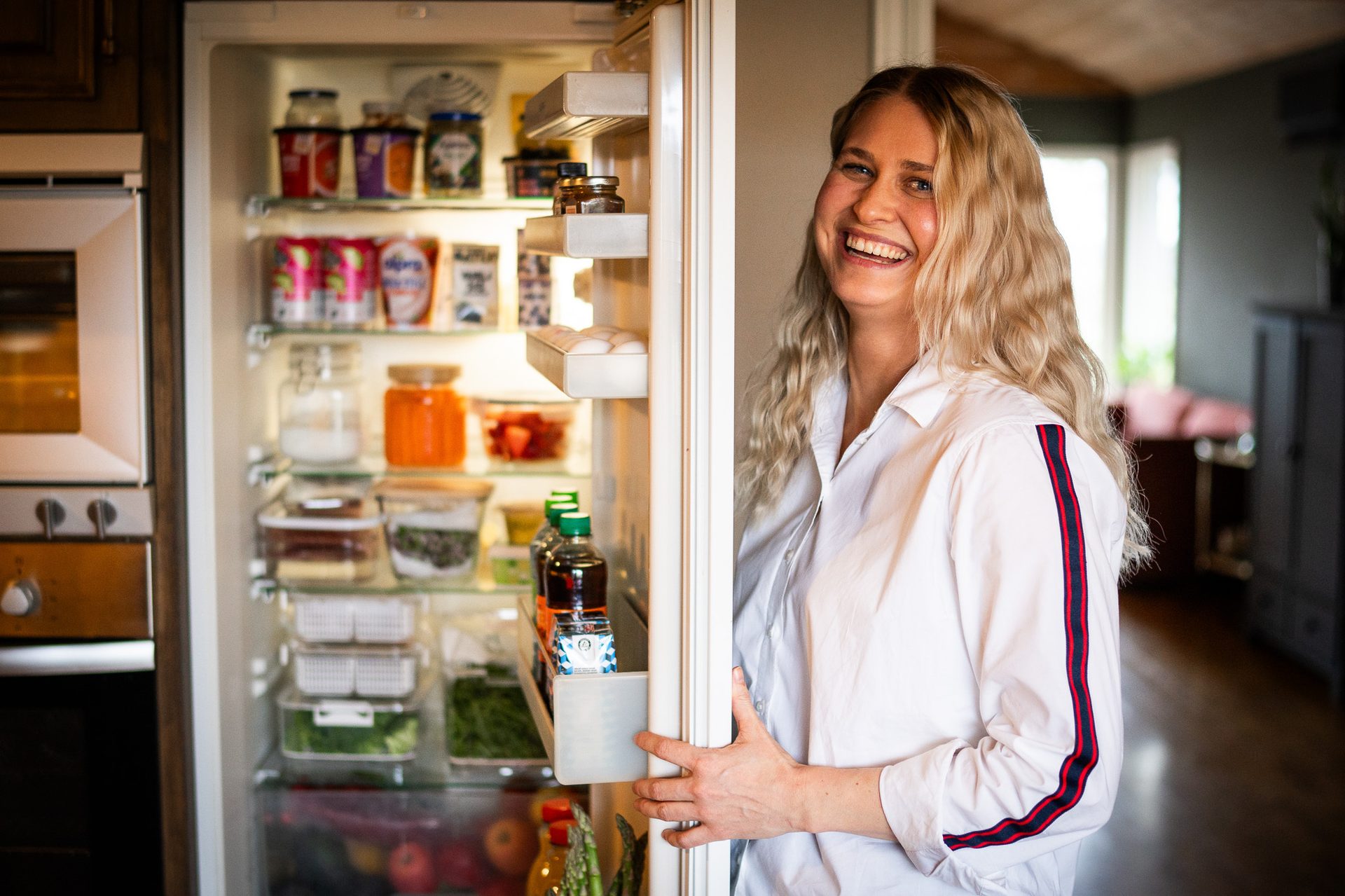 kjøpmann gerd står foran et åpent kjøleskap og smiler