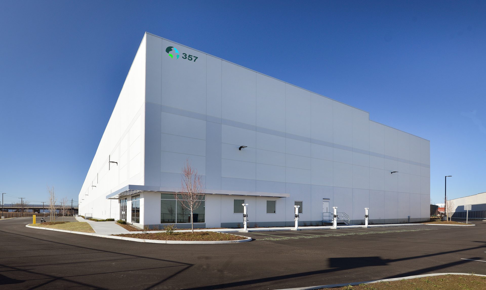 Modern industrial building with a logo and number 357 on its facade, and electric vehicle charging stations.