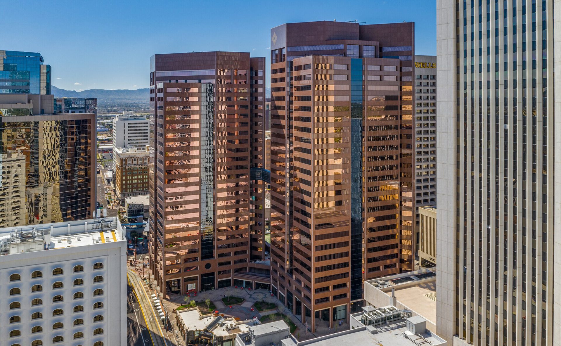 Aerial view of a city with several tall, reflective brown and white skyscrapers under a clear blue sky.