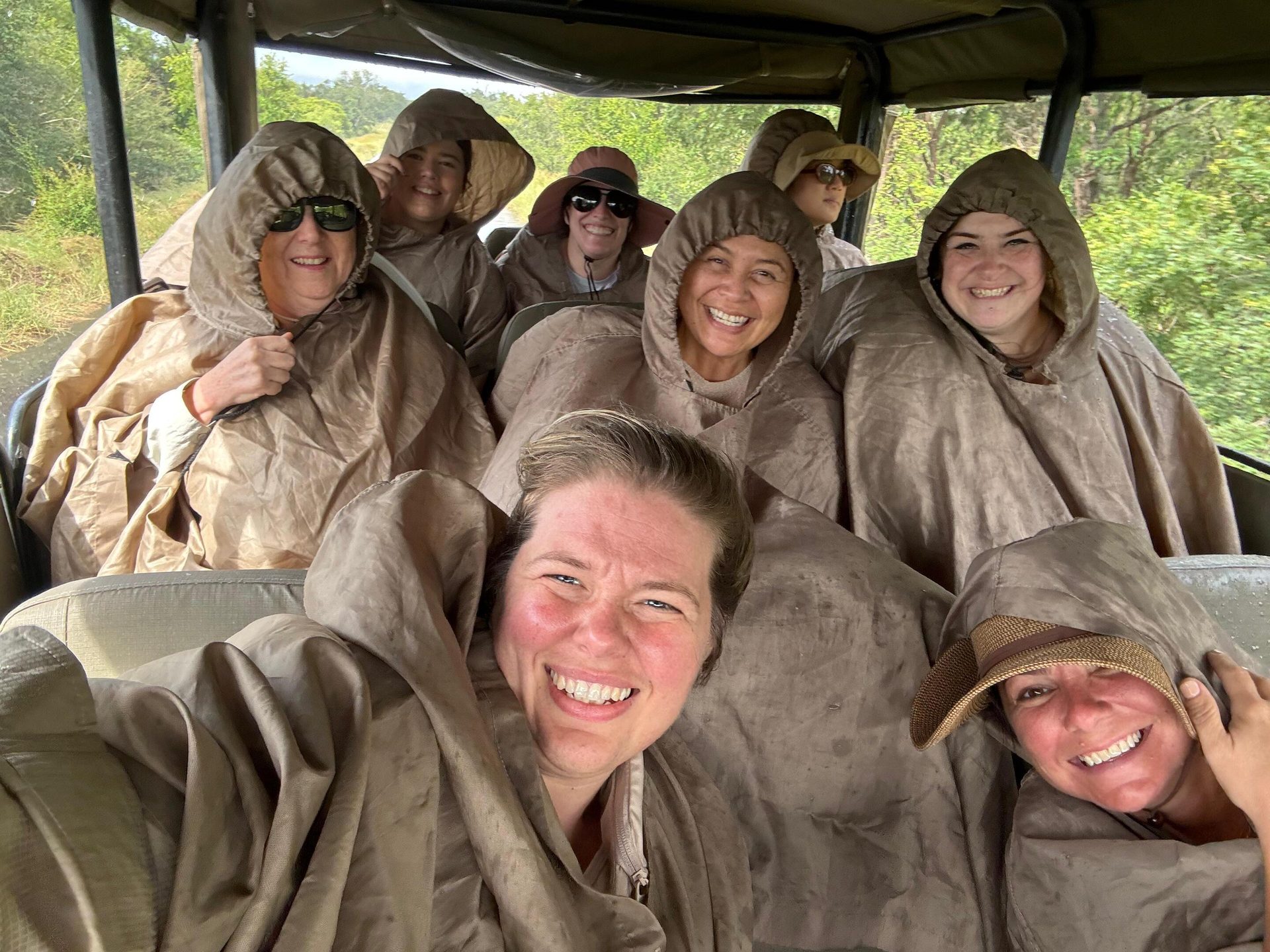 Group of happy women in ponchos riding in an open vehicle during a safari or outdoor adventure.