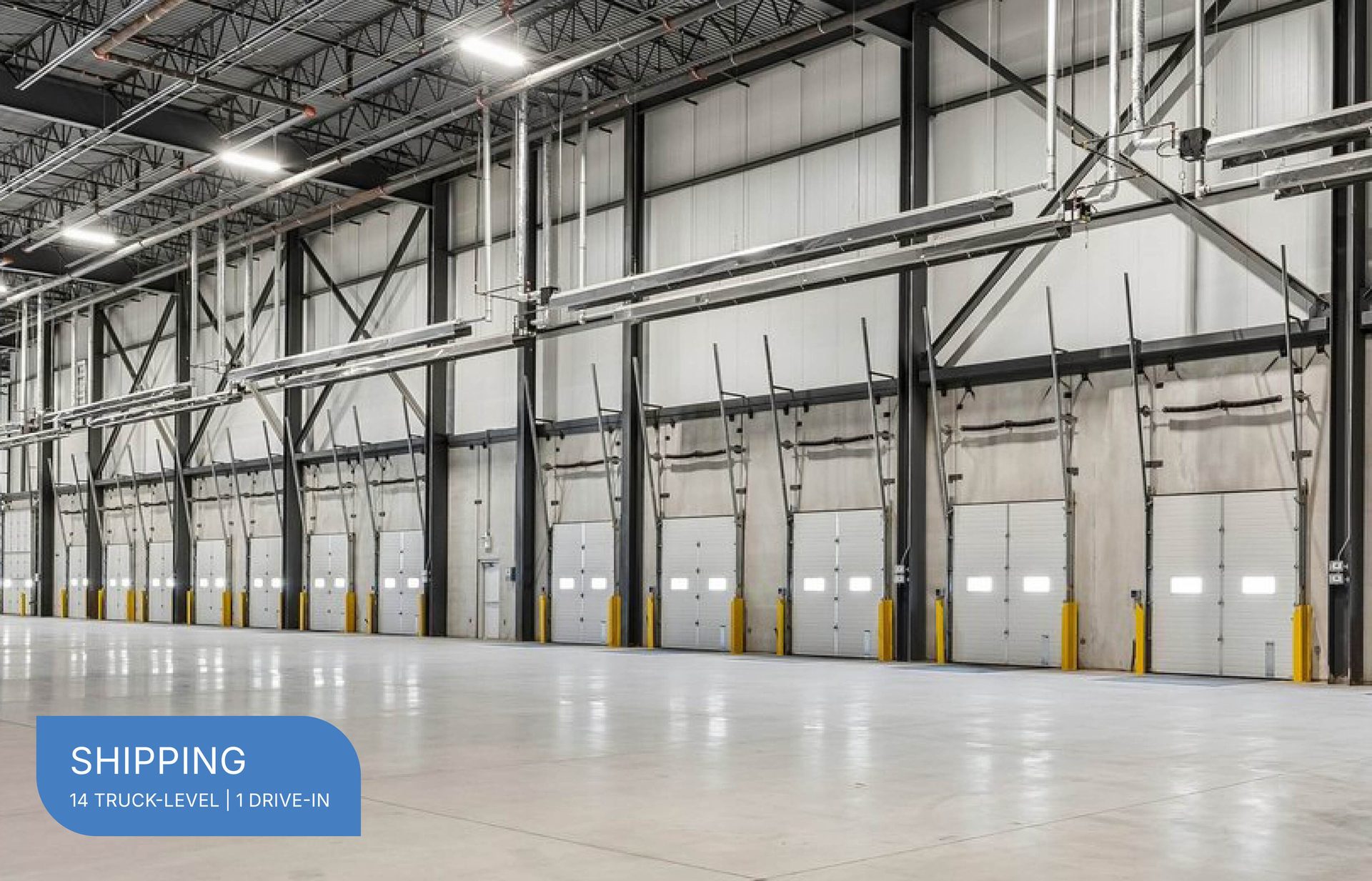 An empty, bright warehouse interior featuring a long row of numerous truck-level loading dock doors and high ceilings.